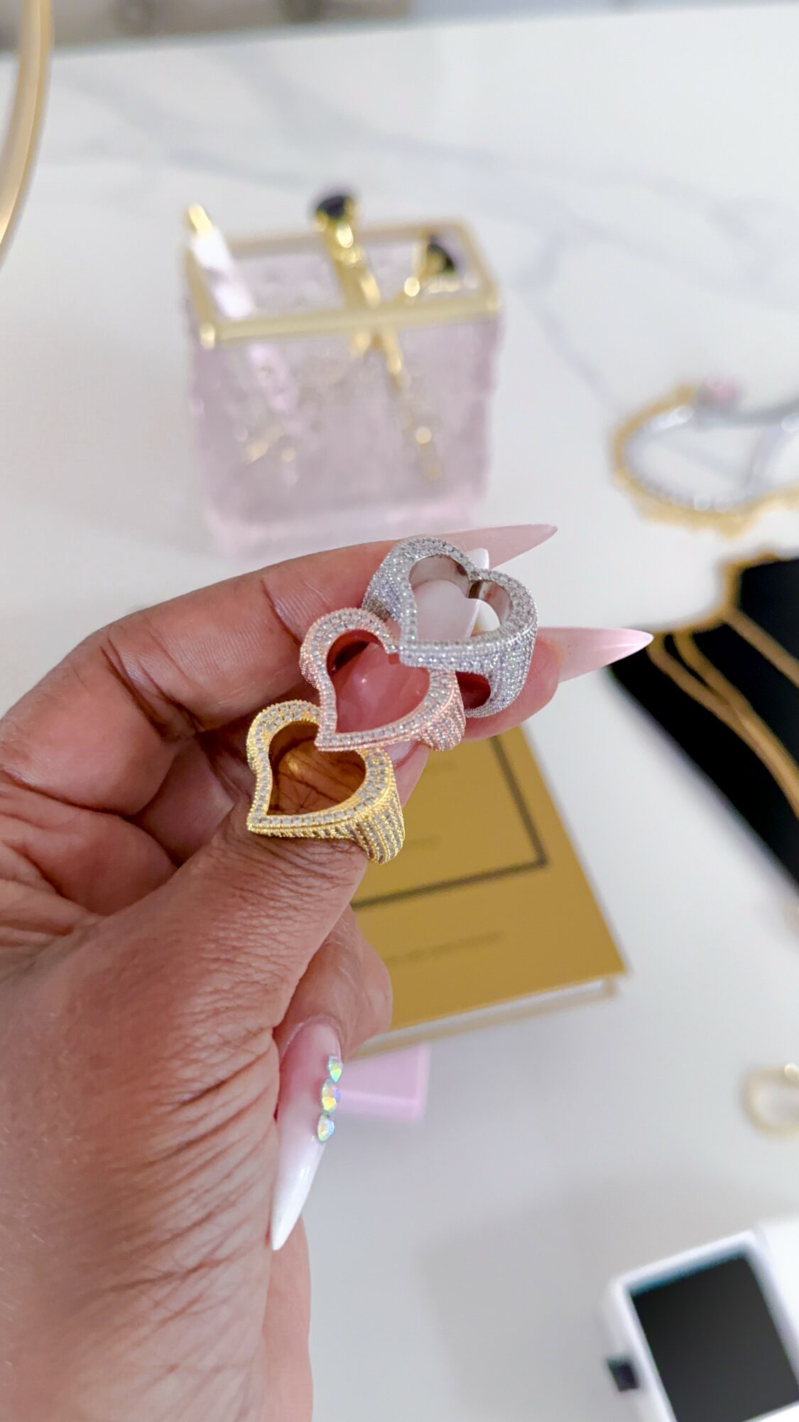 Hand holding three colorful heart-shaped hair clips with a marble-patterned background and jewelry in the background.