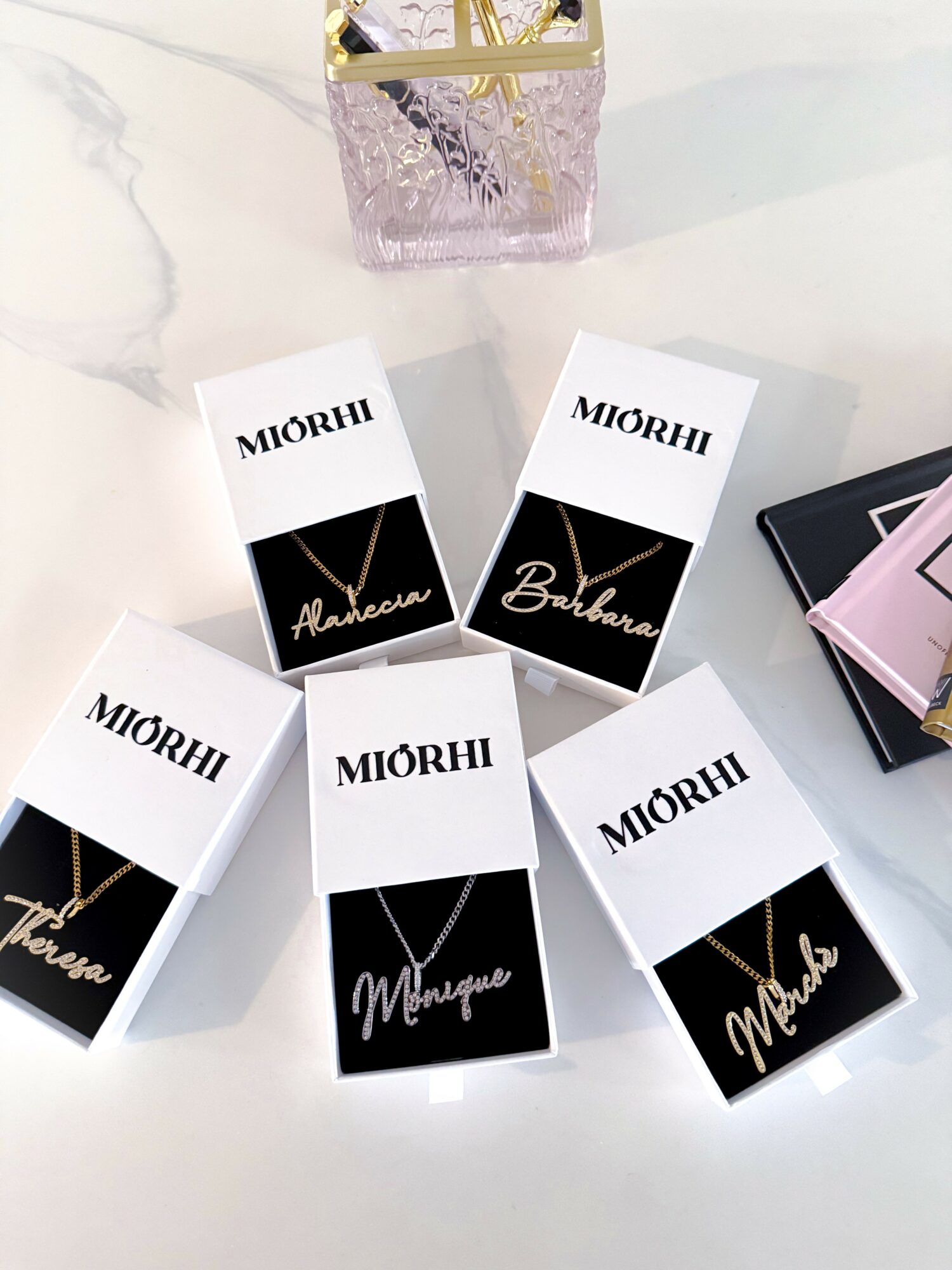 Six boxes with black and white packaging, some with gold text, arranged on a white surface with a pink and gold decorative item above.