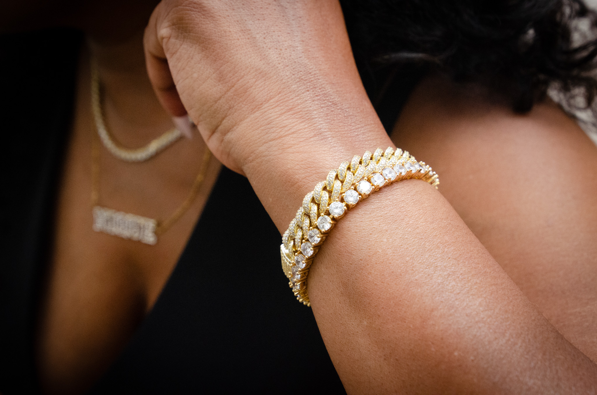 Close-up of a woman's arm with pearl bracelets, part of her black dress and jewelry visible