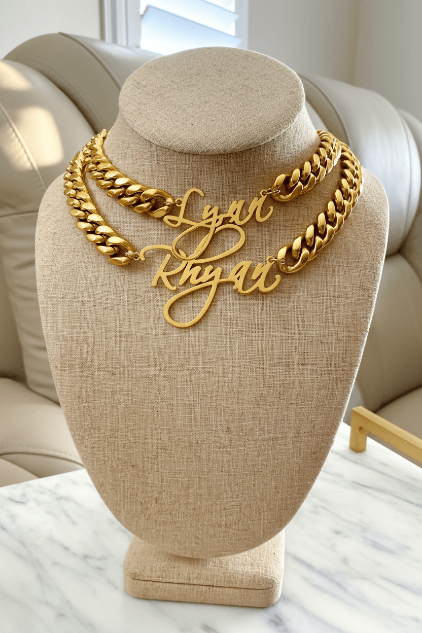 Beige necklace display with two gold chain necklaces, one with a name pendant, on a beige stand in a bright room.