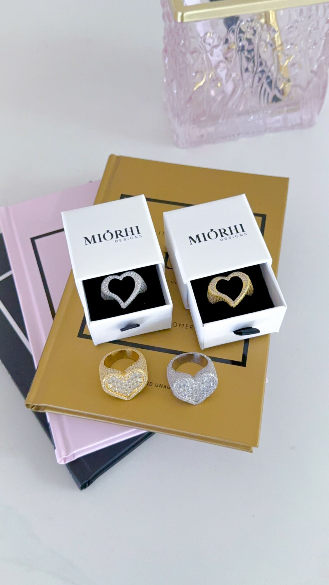 Two boxes of rings, one with a black heart and the other with a gold heart, on a gold book.
