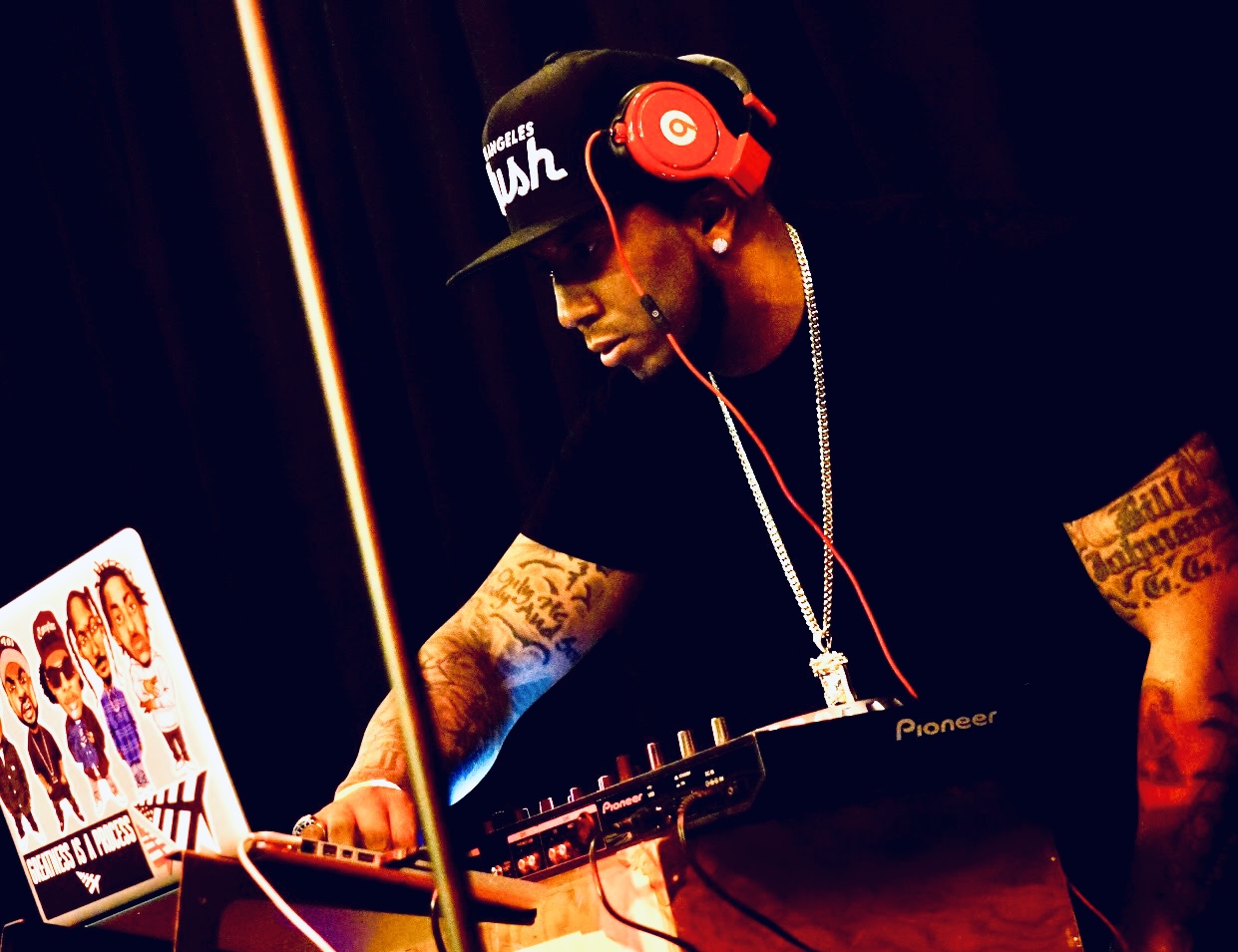 DJ wearing headphones and a cap, working with music equipment in a dark setting.
