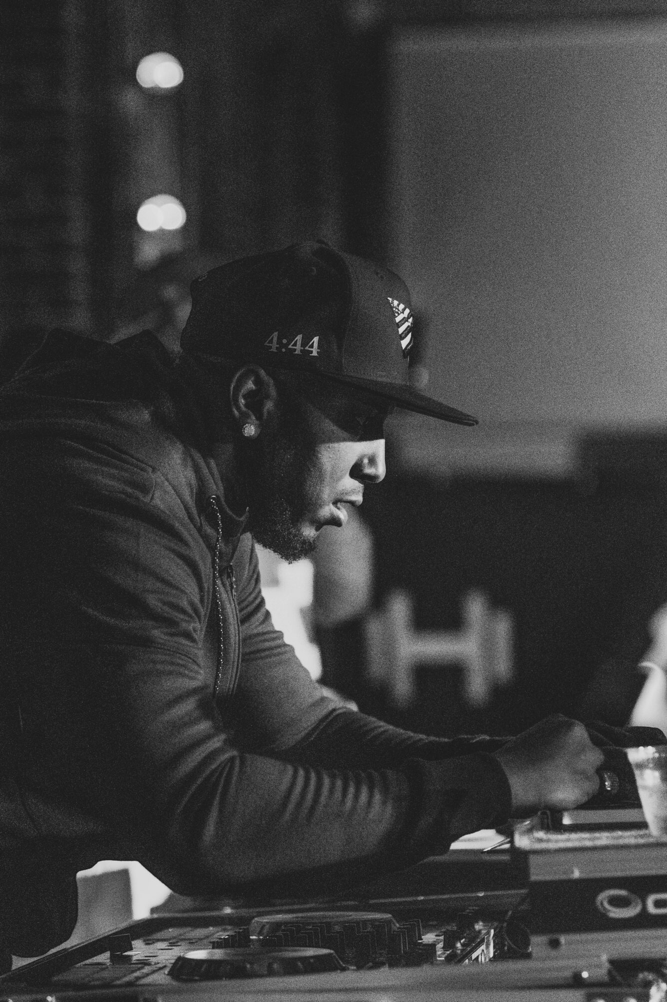 Man wearing a cap and headphones, focused on DJ equipment in a dark setting.