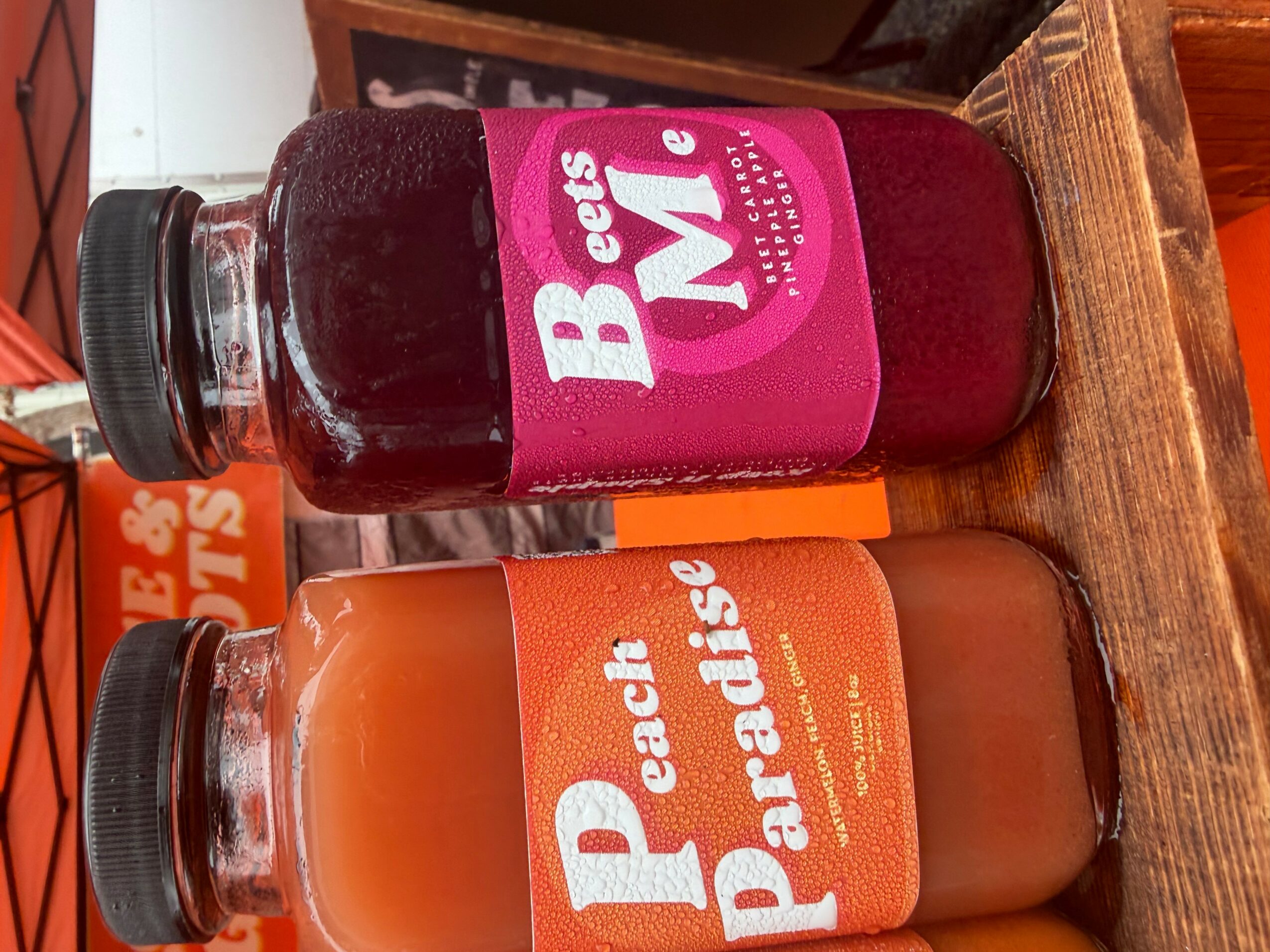 Two bottles of juice on a wooden surface, one with a pink label and the other with an orange label.
