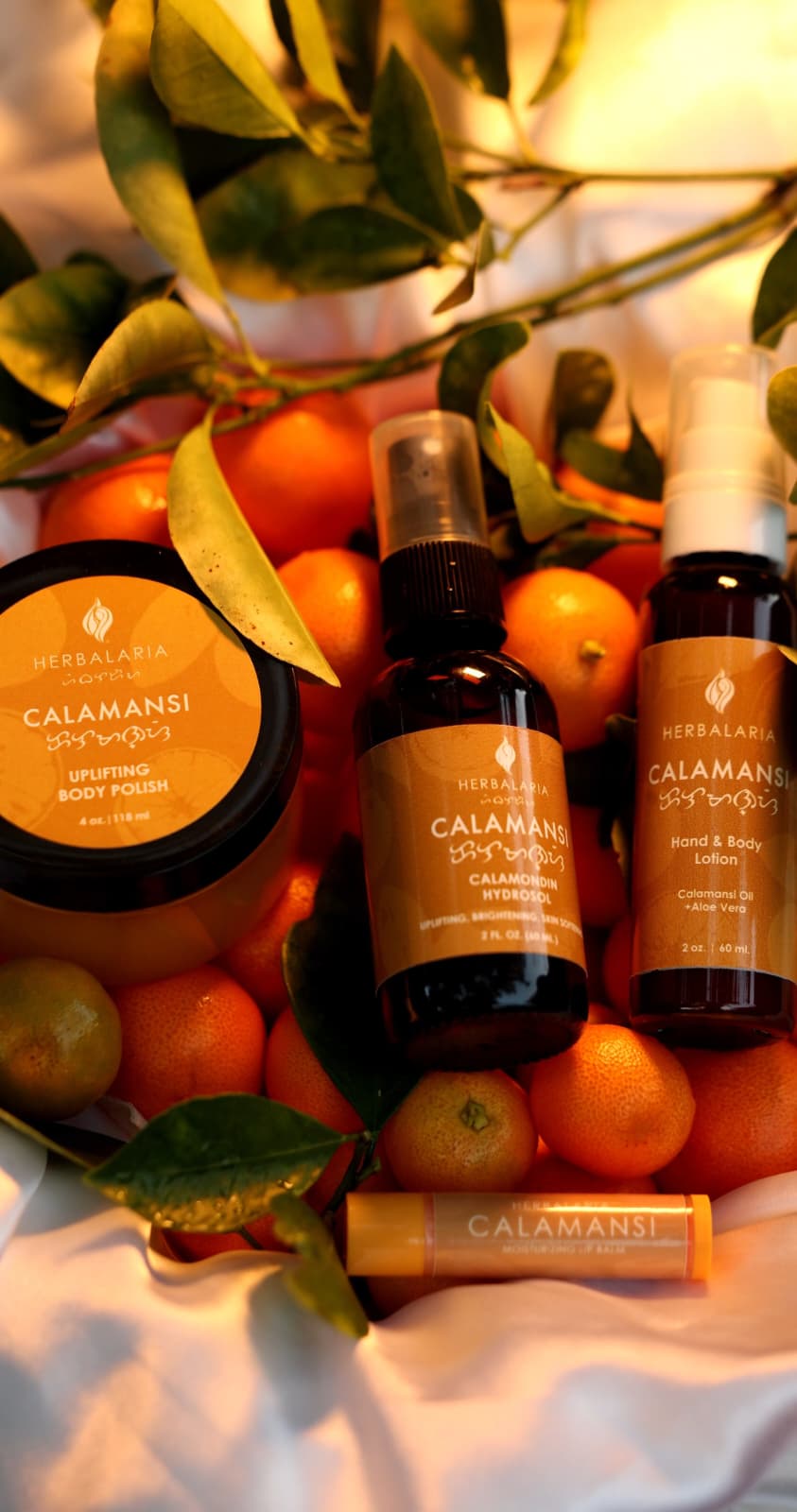 Assorted Calamansi skincare products surrounded by calamansi fruits and green leaves, on a white surface.
