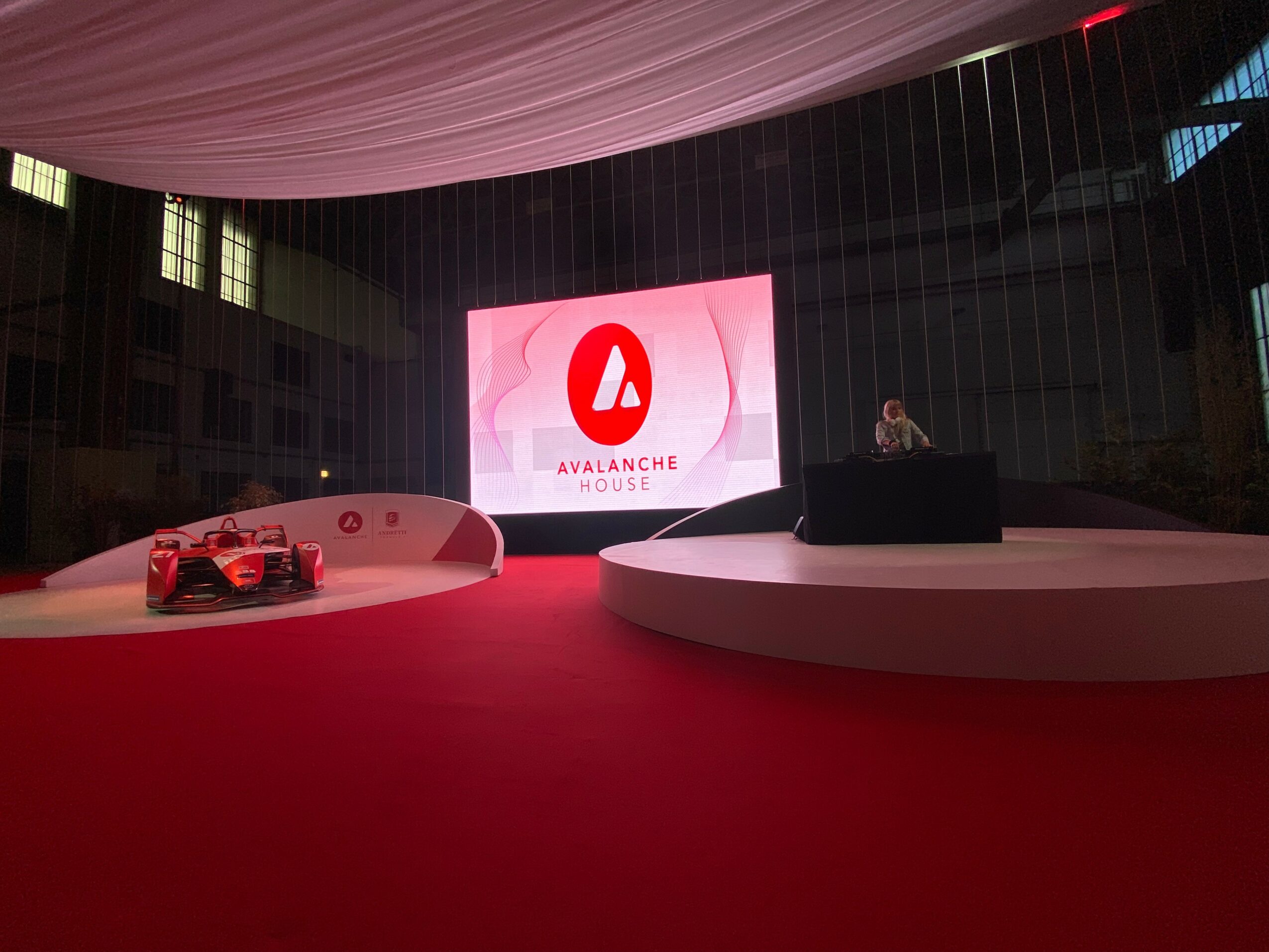 Stage with a large screen displaying the Avalanche logo, a car on the left, and a person at a podium on the right.