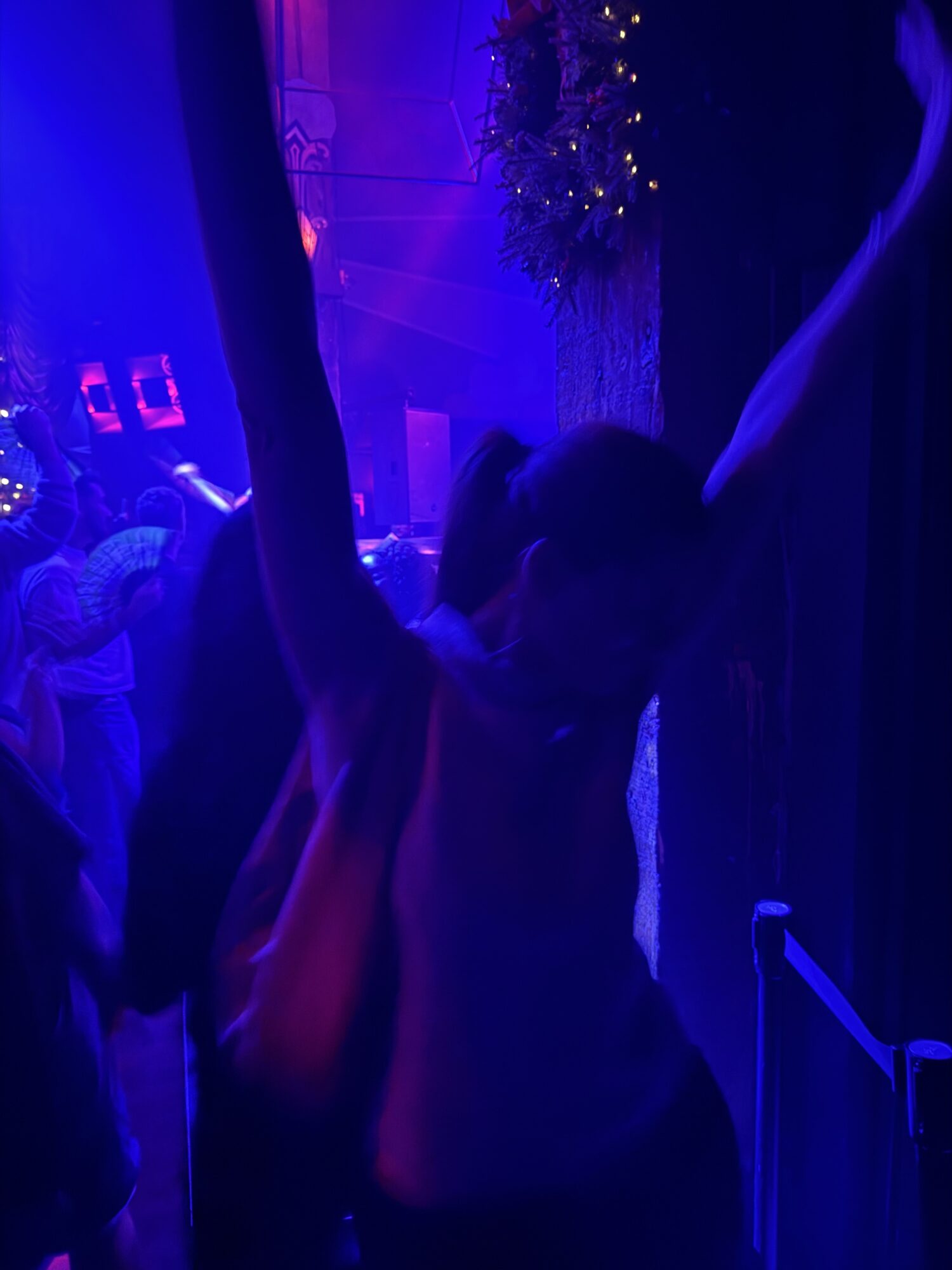 Person sitting in a dark room illuminated by blue and purple lights, with a hand extended outward.