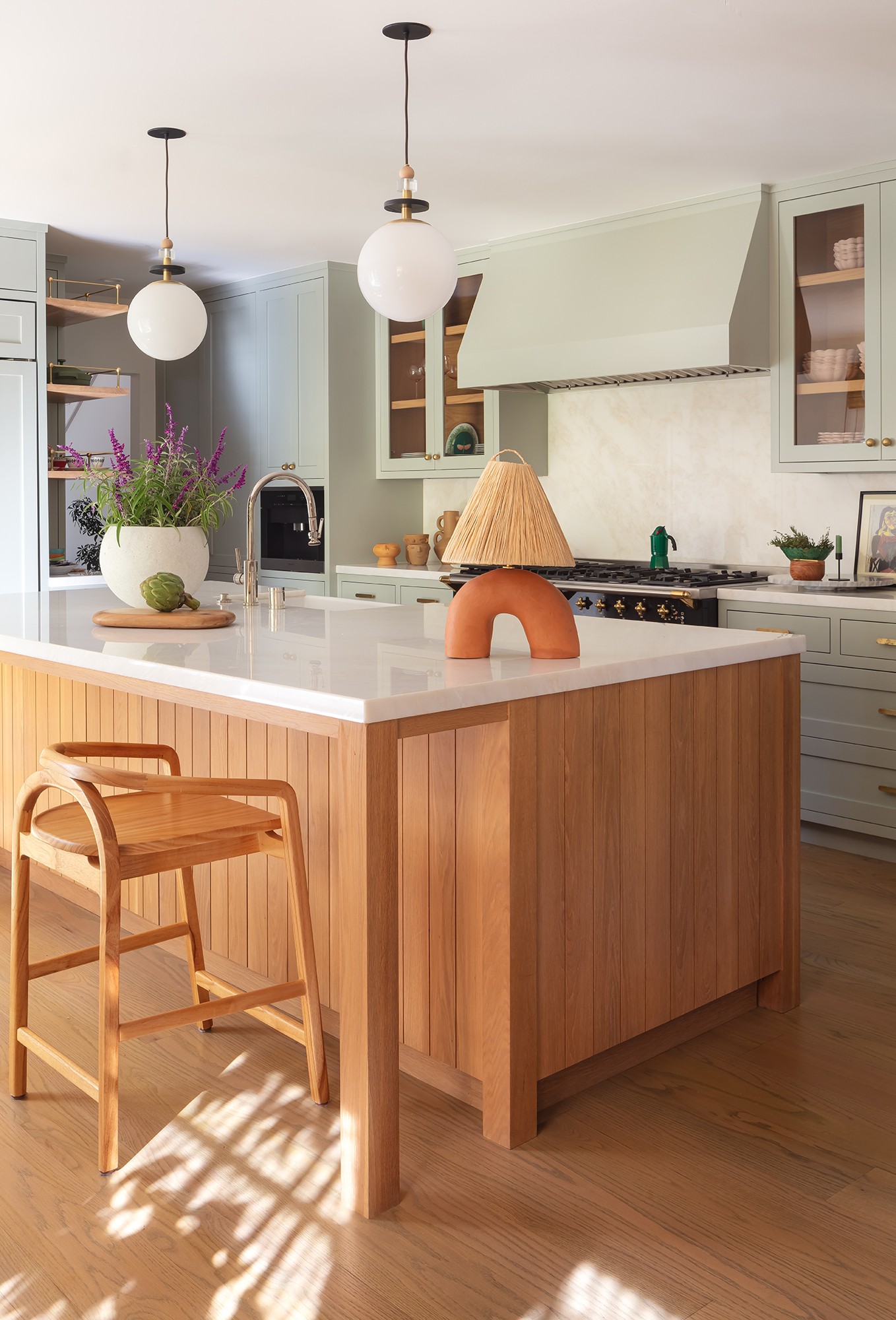 Kitchen with island, wooden chair, hanging lights, and cabinets, sunlight through window, neutral colors, modern design.
