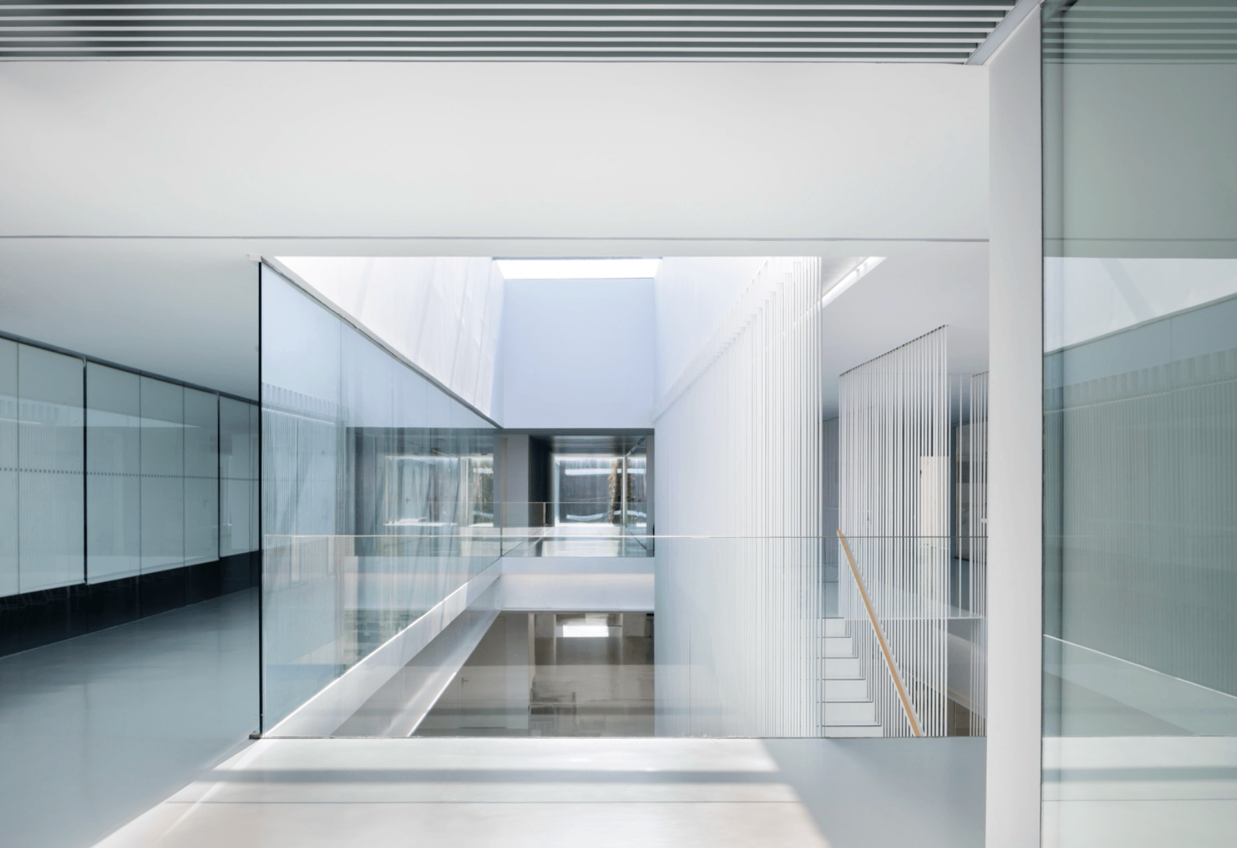 Modern interior with glass walls, white surfaces, and a central open space, featuring clean lines and minimalistic design.