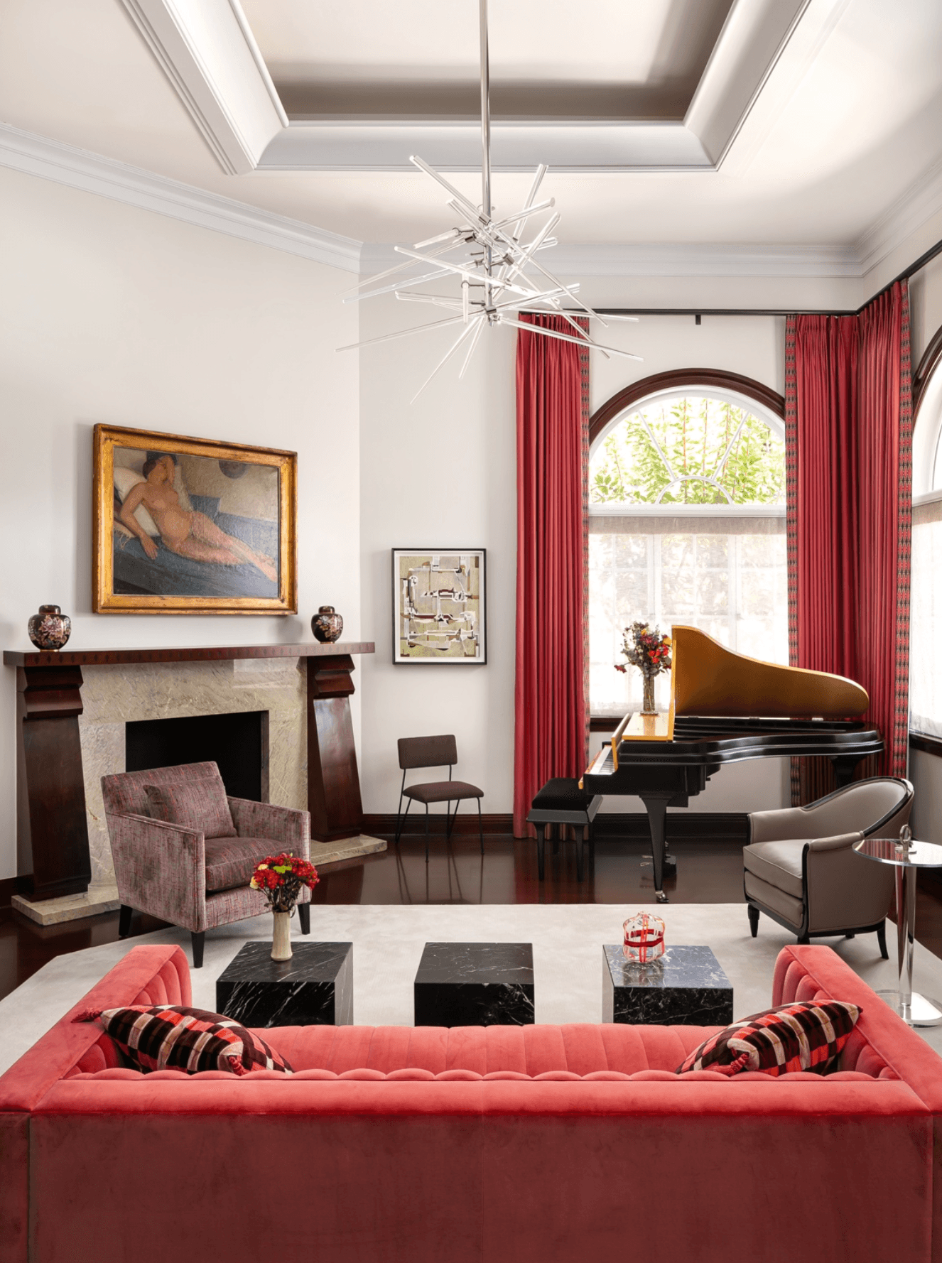 Living room with a grand piano, red curtains, a pink sofa, and a fireplace with artwork above, bright natural light.