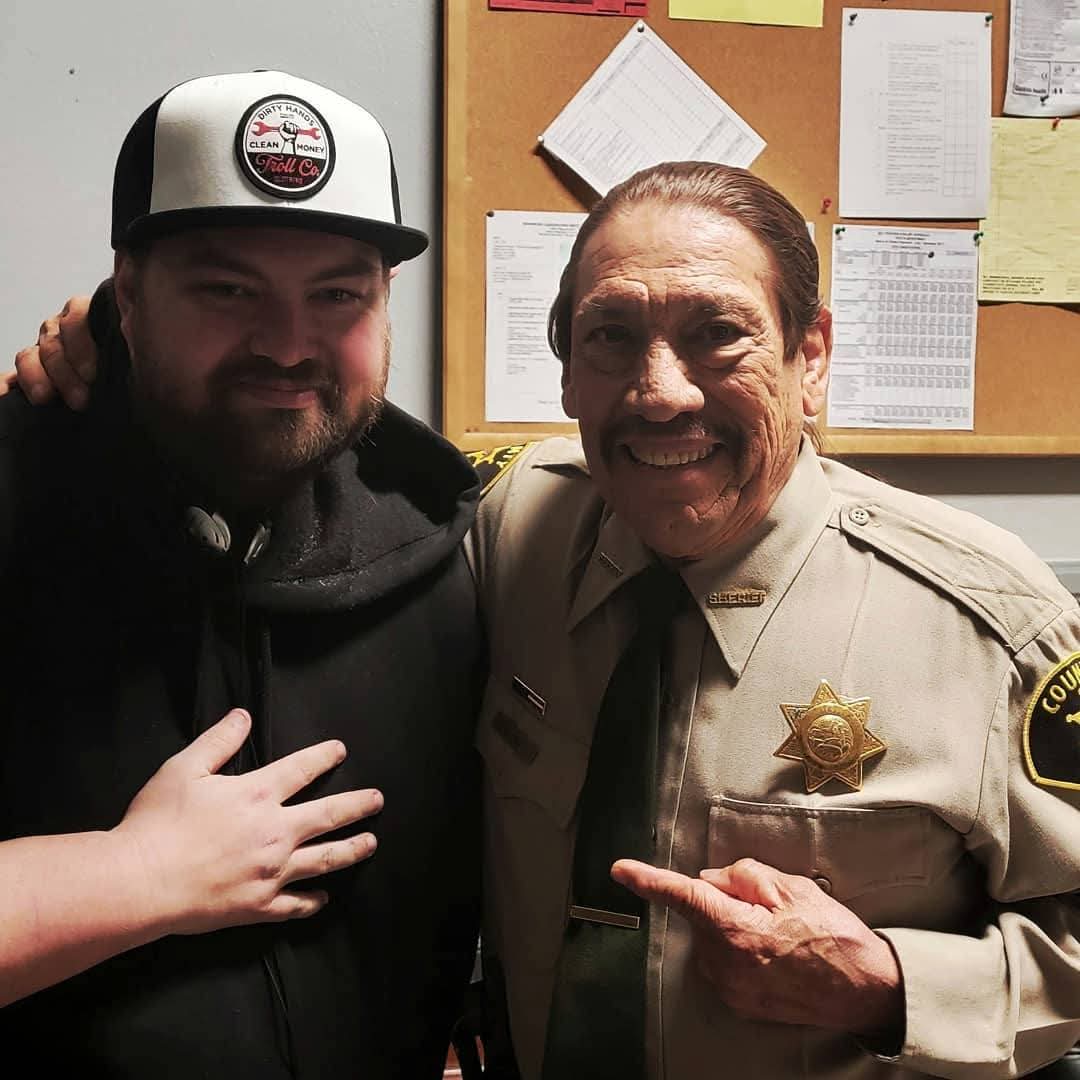 Two men smiling, one in a police uniform and the other in casual clothing, standing close together indoors.