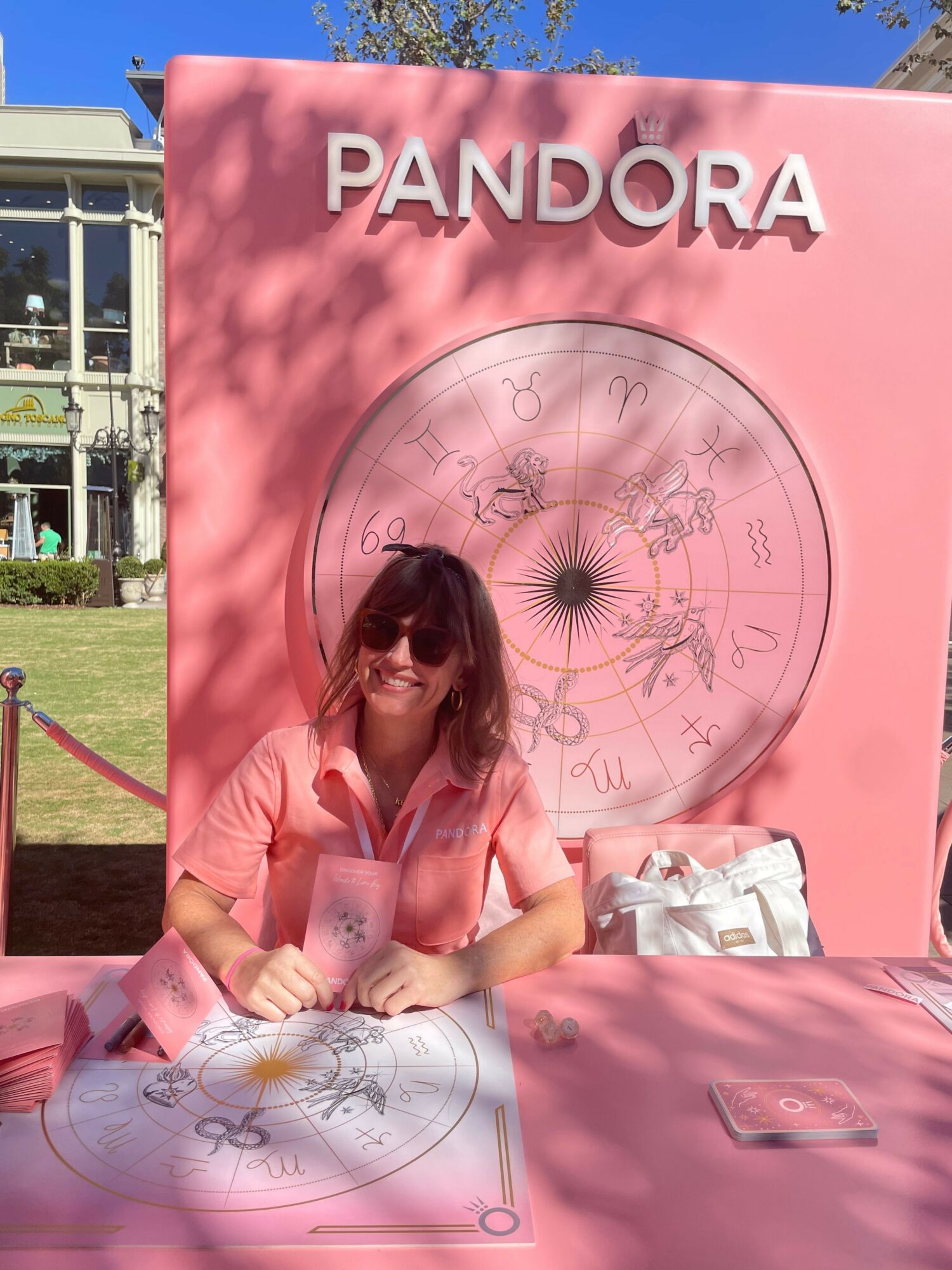 Person sitting in front of a pink Pandora display with a large circular clock and pink background, holding a shopping bag.