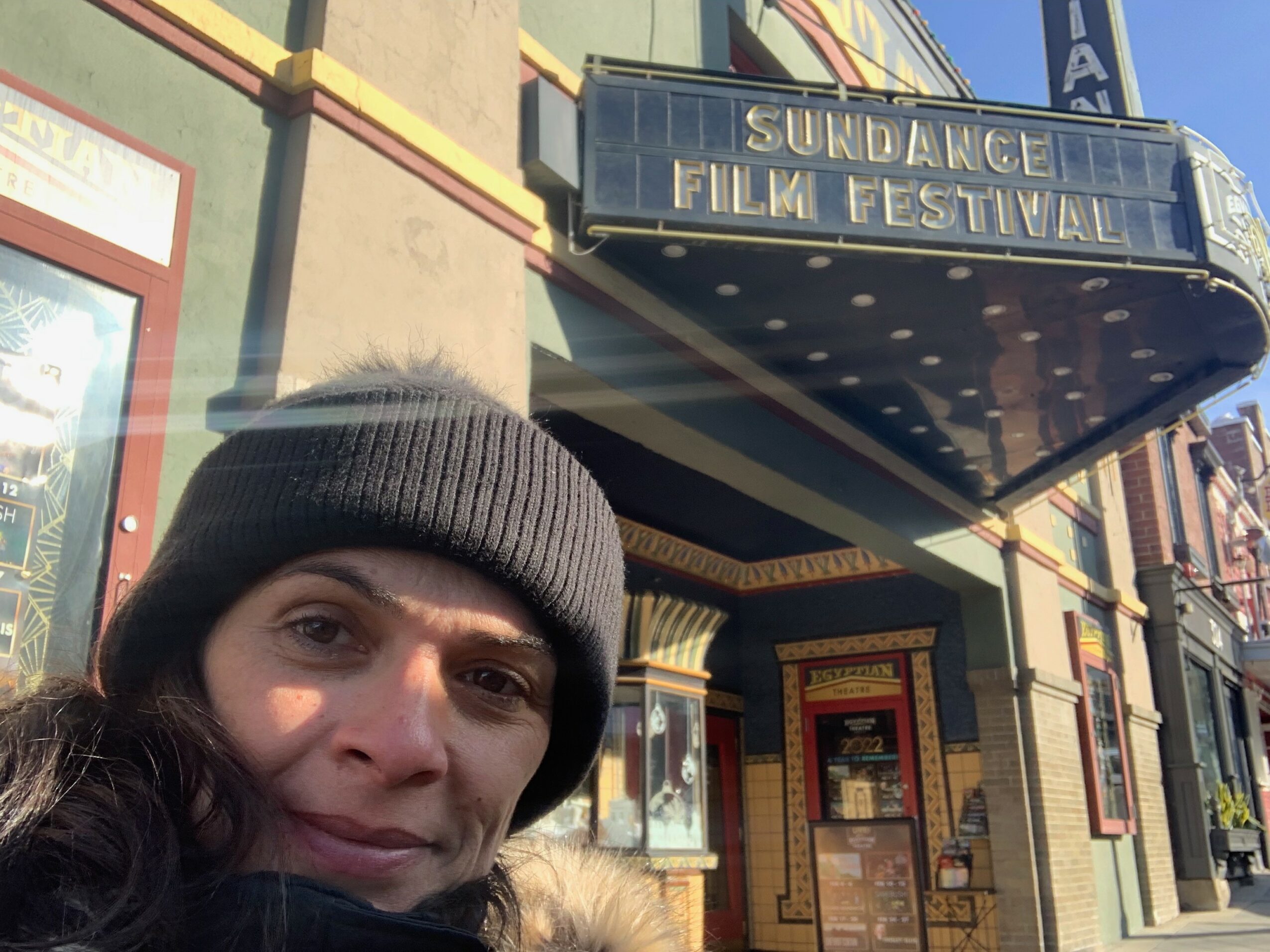 Woman wearing a beanie hat standing outside a building with a marquee sign for a film festival.