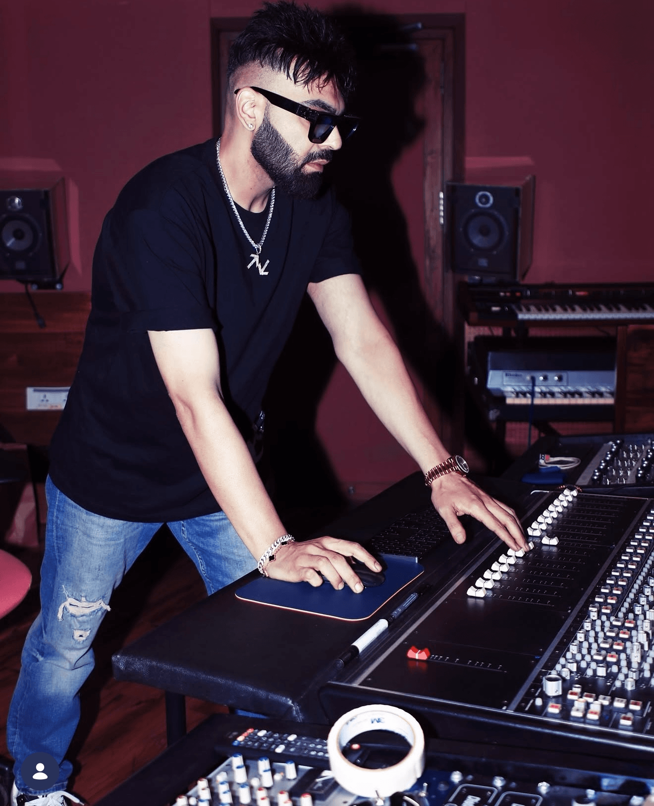 Person with sunglasses and jewelry operates music equipment in a studio.