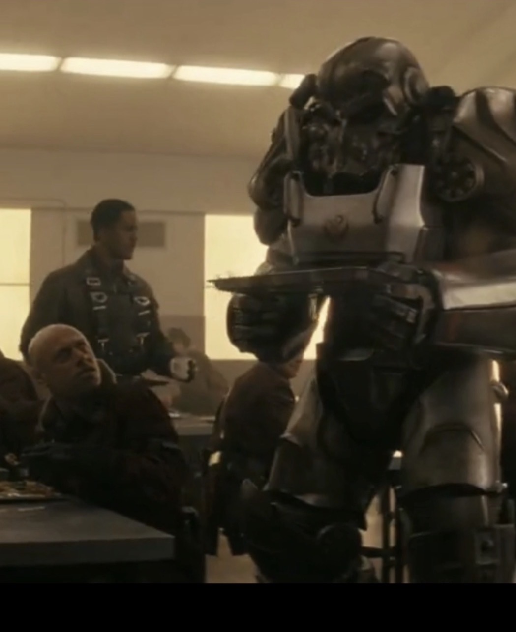 A person in a robot costume interacts with a group of people in a room with bright overhead lighting.
