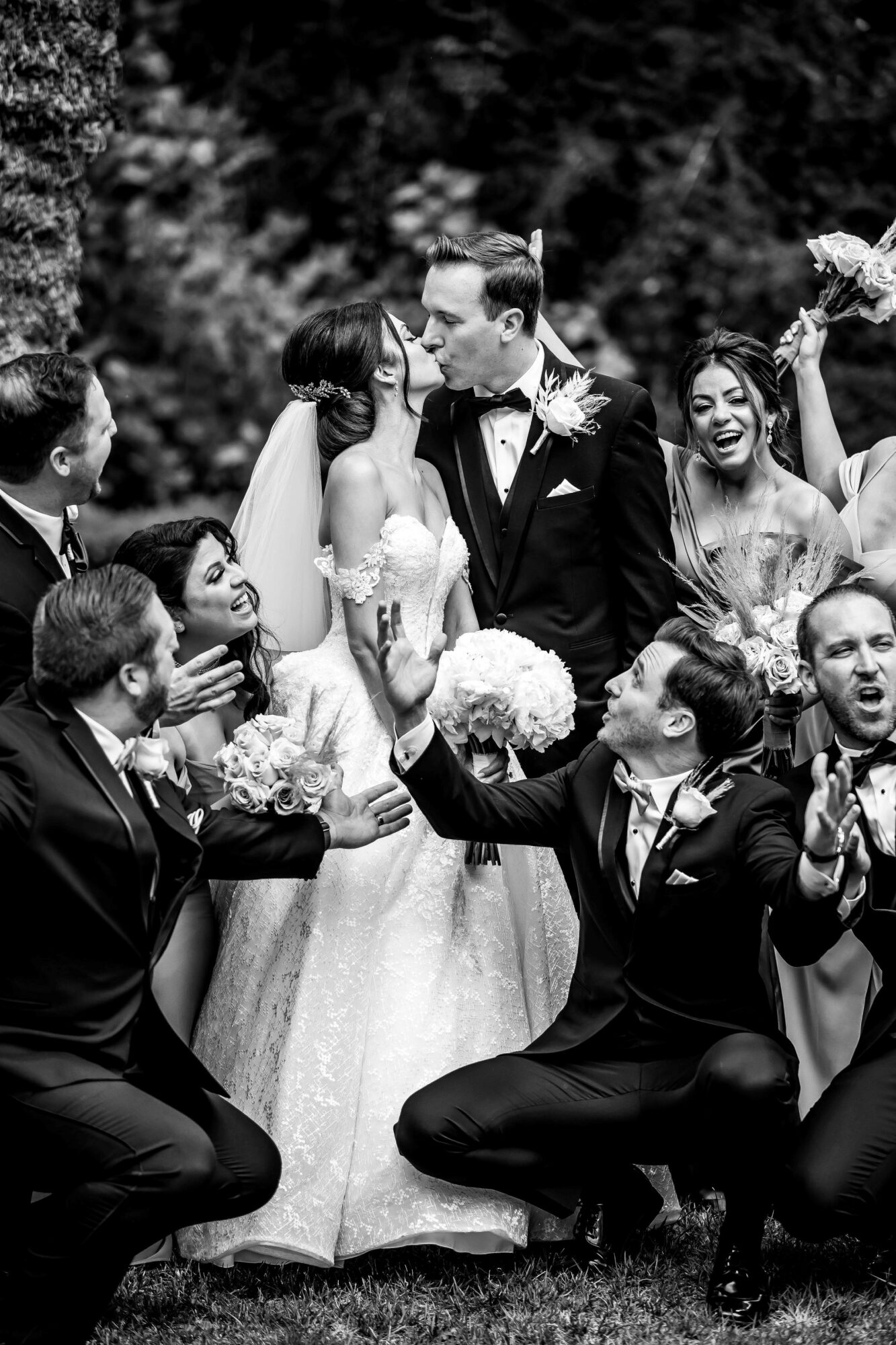 Group of people celebrating outdoors, with a bride and groom in the center, surrounded by friends, some clapping and smiling.