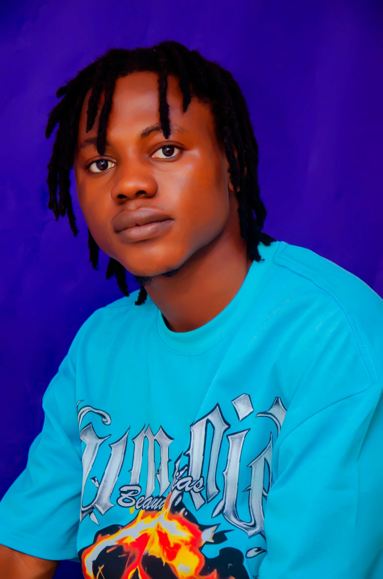 Young person with dreadlocks wearing a bright blue T-shirt against a purple background.