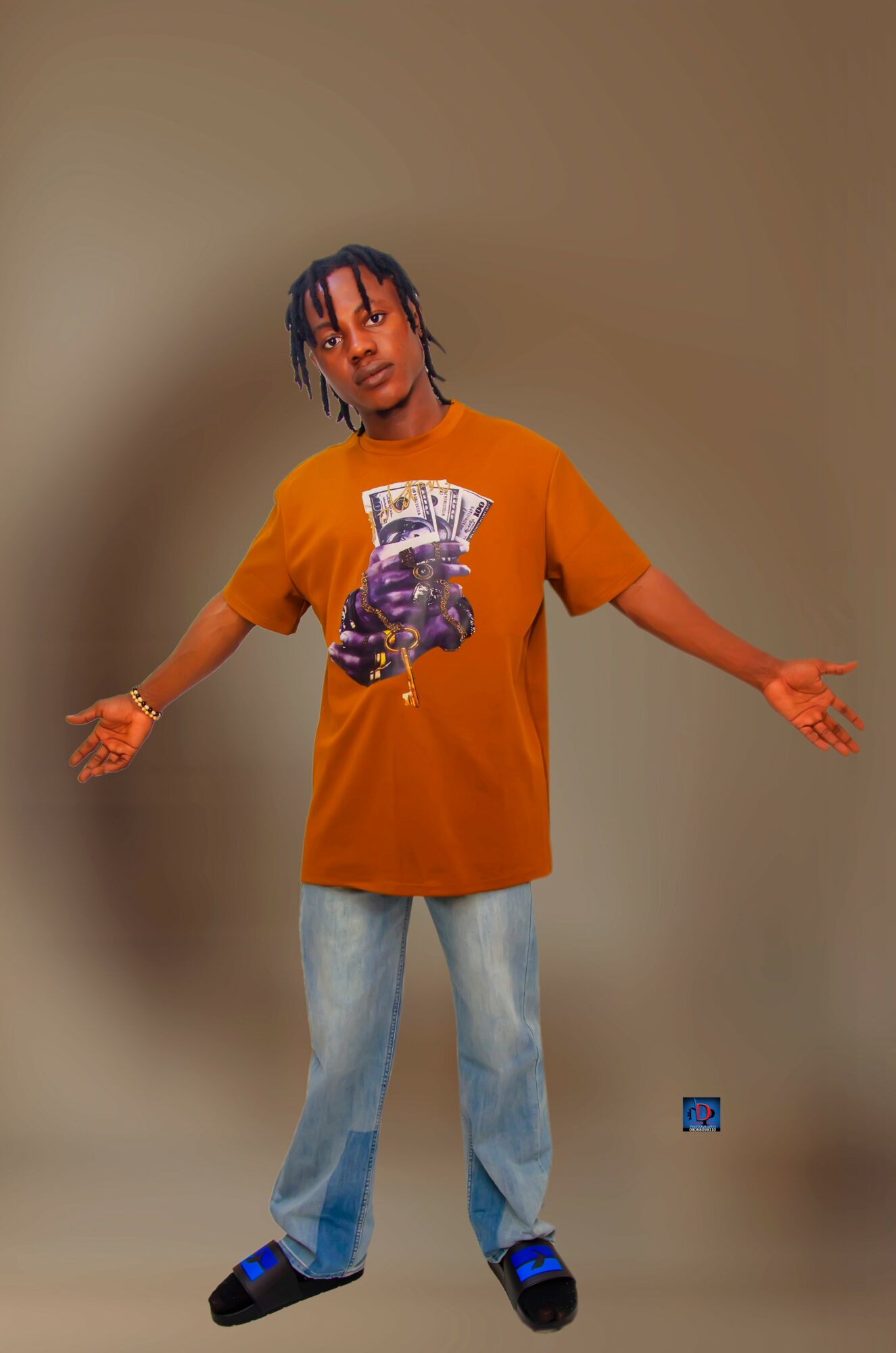 Person with arms outstretched, wearing an orange T-shirt with a graphic, light blue jeans, and black shoes, standing against a plain background.
