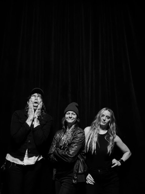 Three women standing in front of a dark curtain, smiling and posing for the camera.