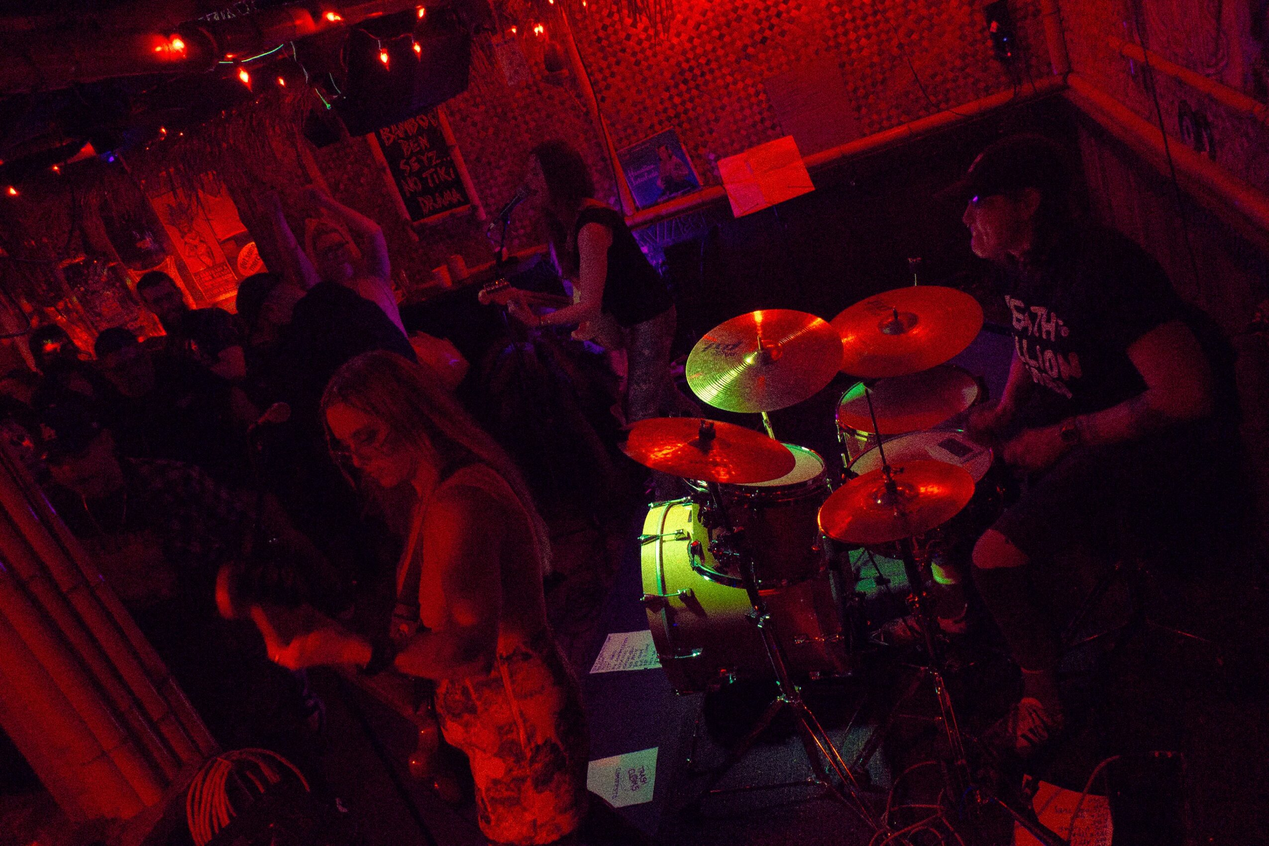 People dancing and playing drums in a dimly lit, red-colored club or party scene.