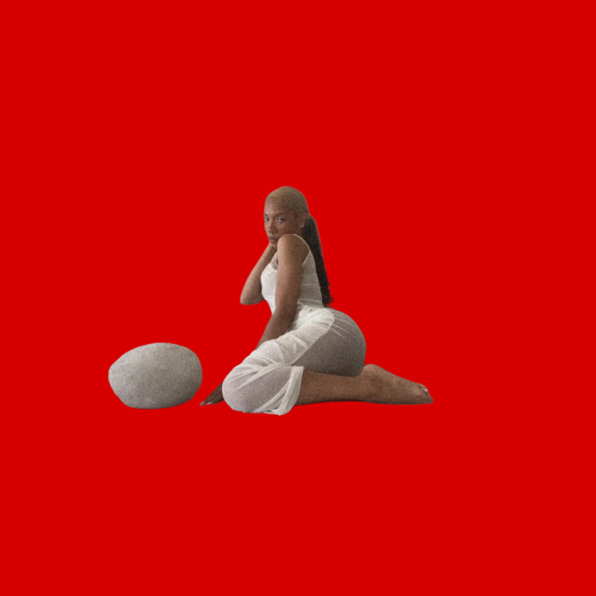 Person with long hair kneeling on the floor, facing sideways, with a large stone nearby, against a red background.