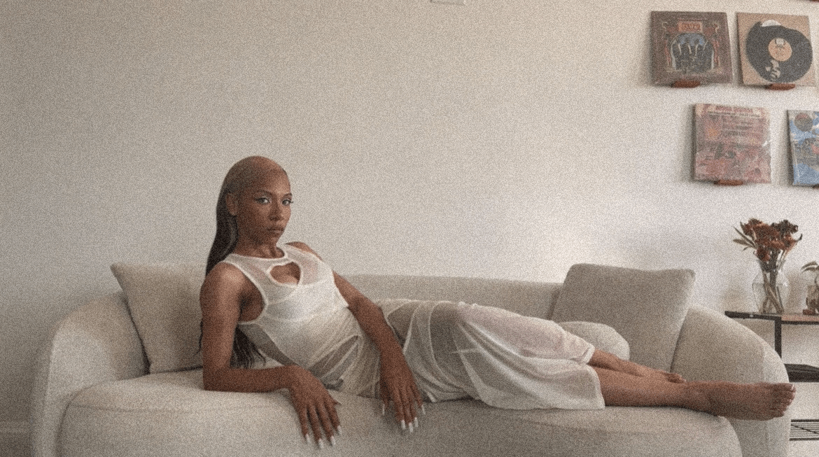 Woman lying on a sofa in a white dress, with artwork on the wall behind her.