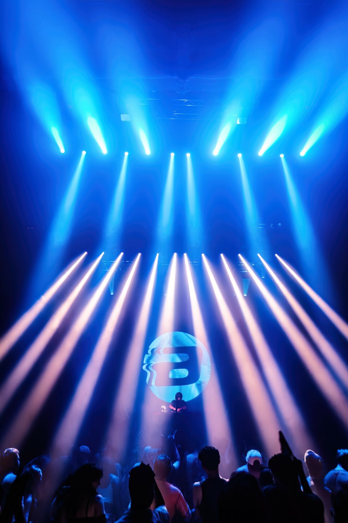 Stage with blue and white lights shining down on an audience, with a circular logo on the floor.