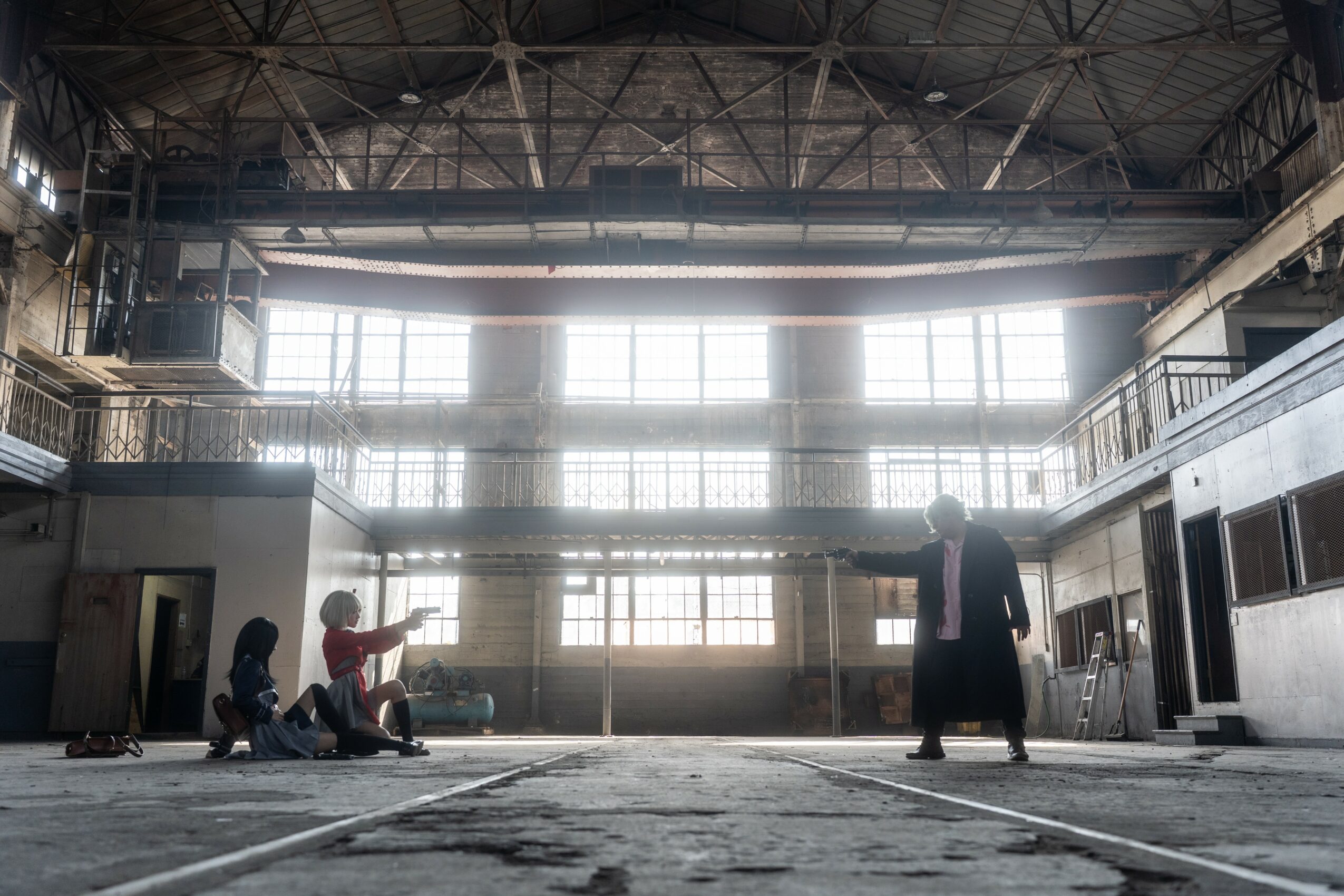 People sitting and standing inside a large industrial building with high windows and metal structures.