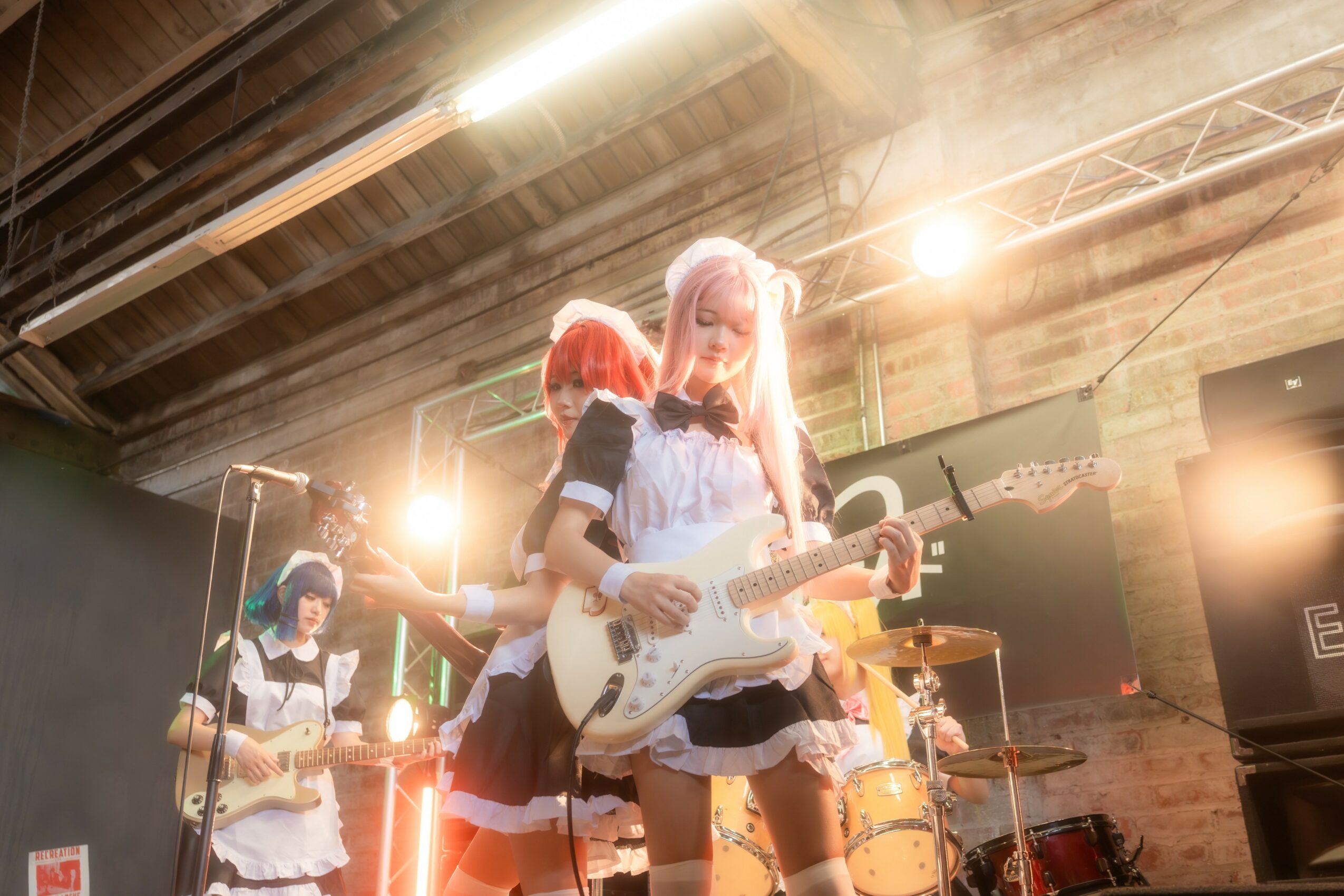 Group of young women playing electric guitars on stage with bright lights and industrial background.