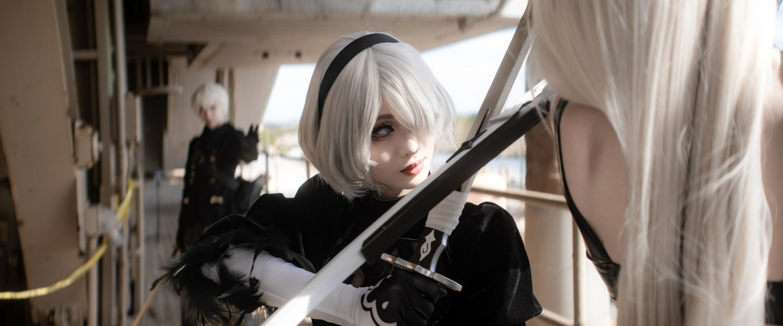 Two people with white hair in costumes, one holding a sword, on a ship or industrial setting.