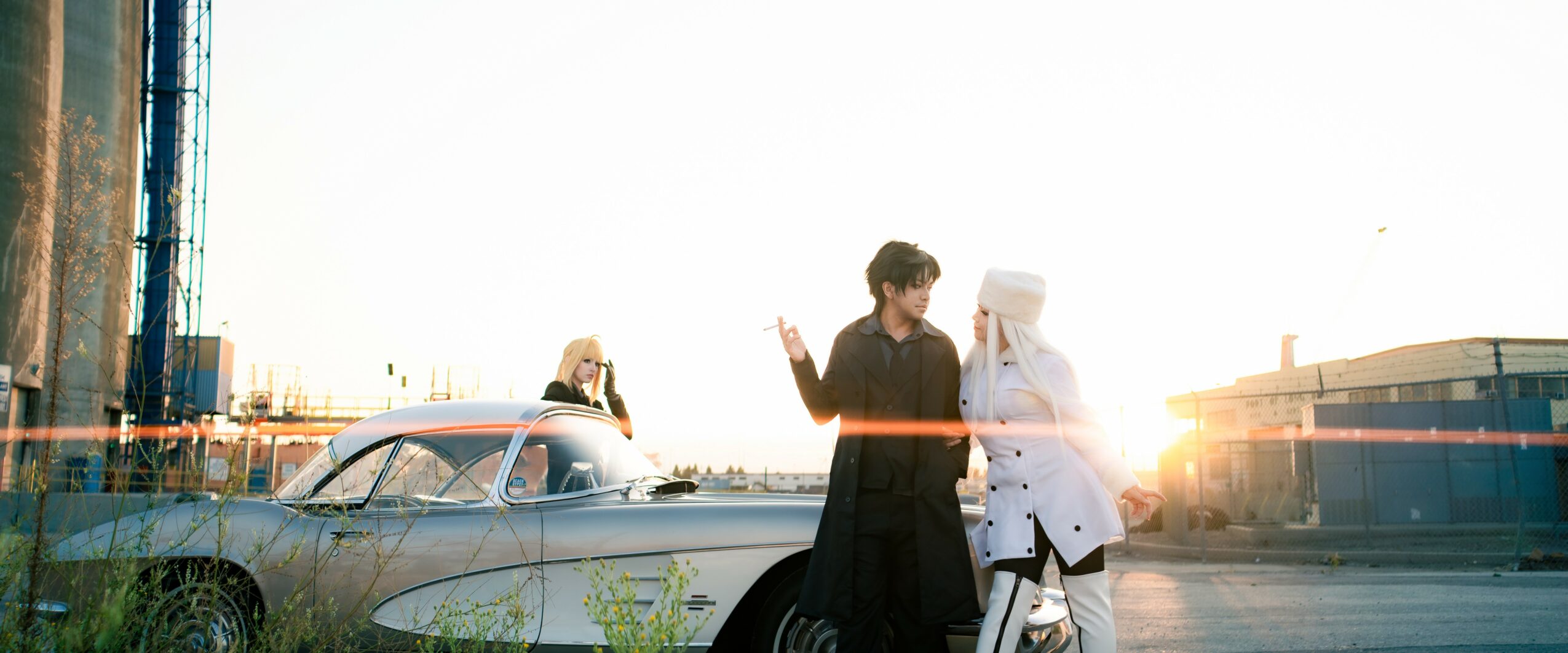People standing near a classic car with a city skyline and sunset in the background.
