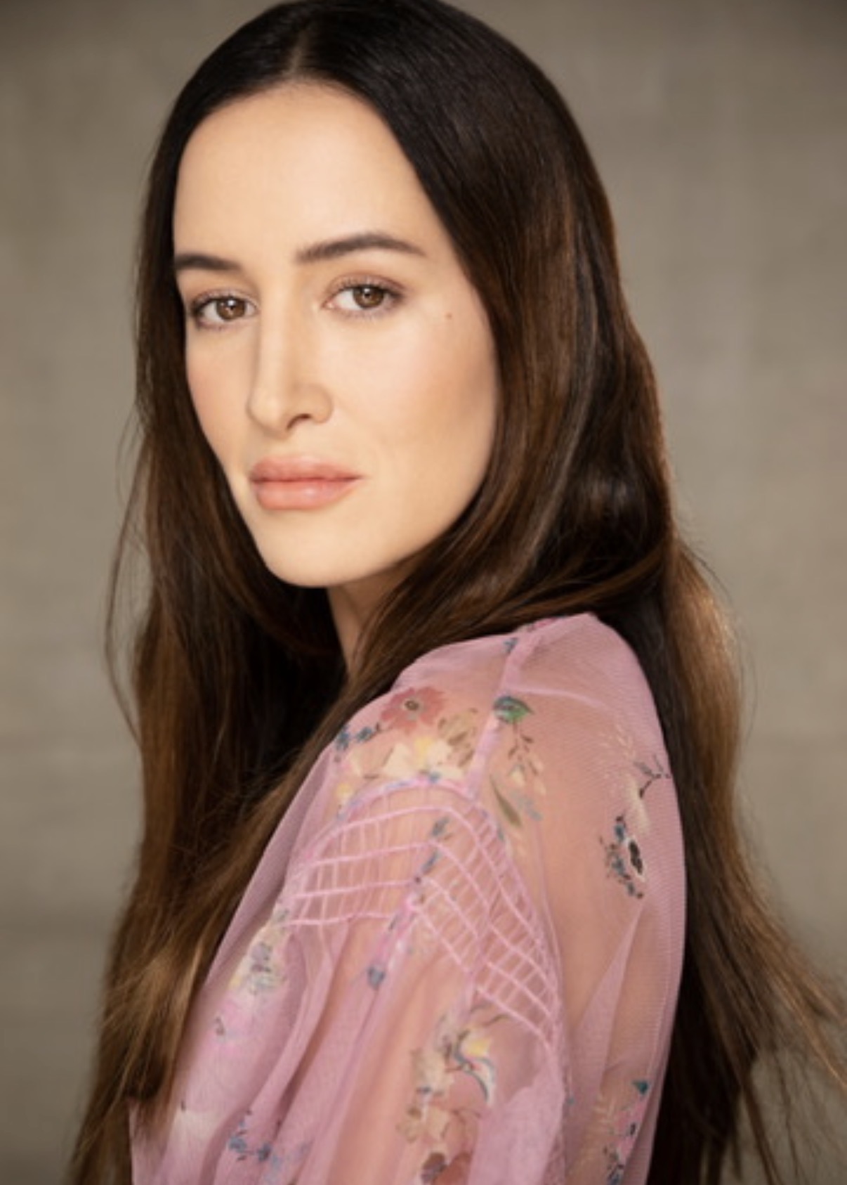 Portrait of a woman with long dark hair, wearing a pink floral top, looking at the camera.