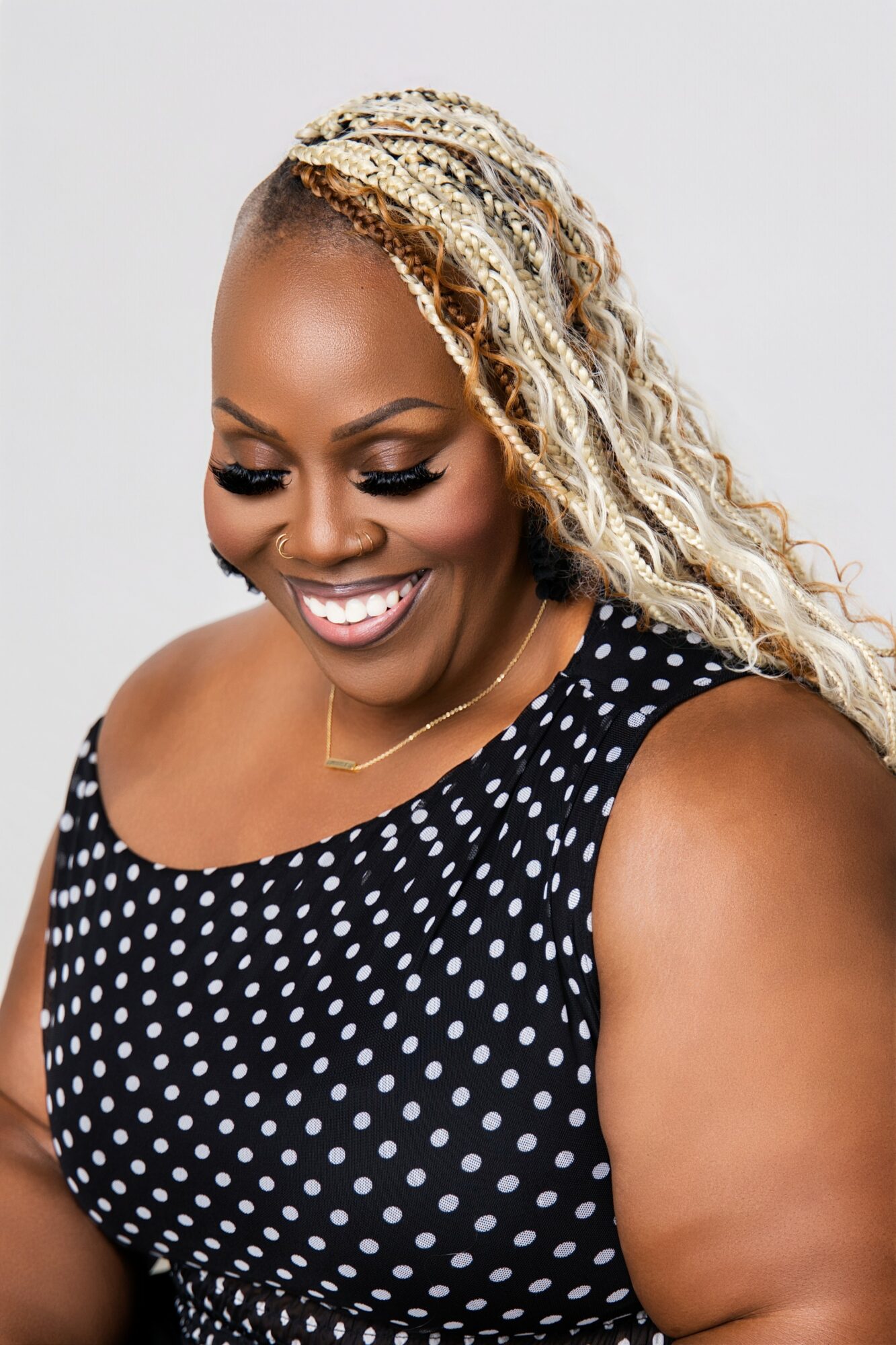 Smiling woman with blonde curly hair wearing a black and white polka dot top, looking down.