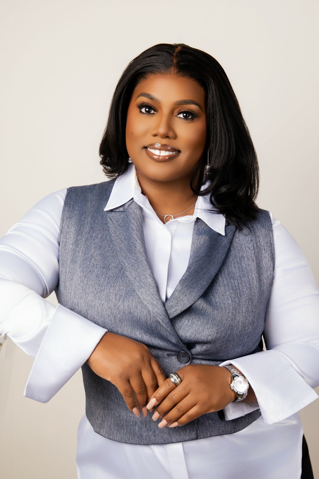 Woman with shoulder-length black hair, wearing a white shirt and gray vest, smiling, against a plain background.