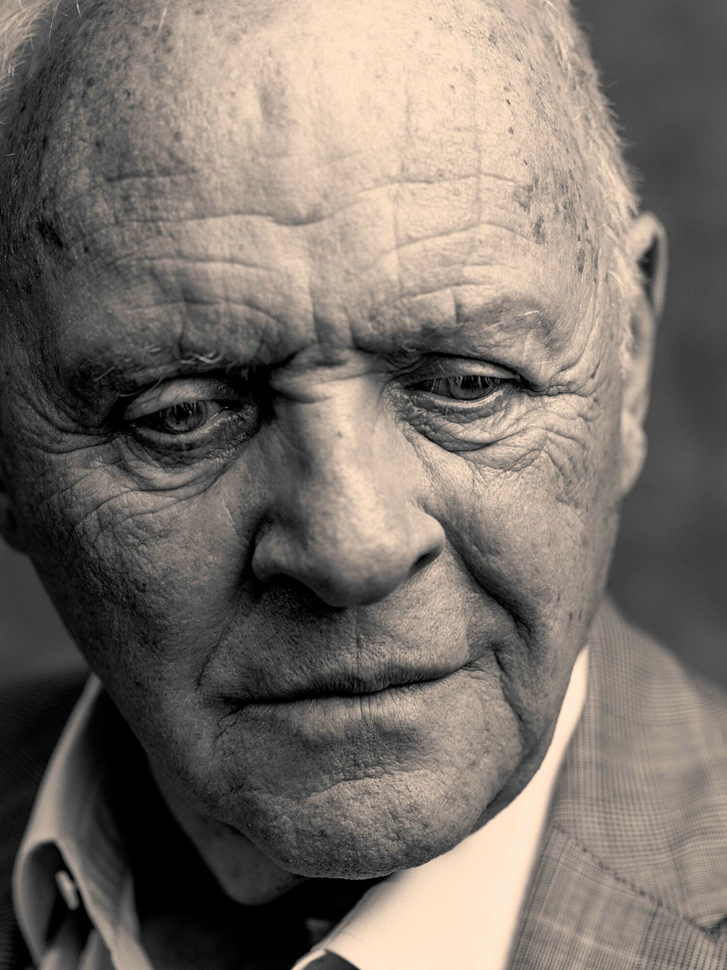 Close-up of an elderly man's face with detailed wrinkles and a contemplative expression, in black and white.