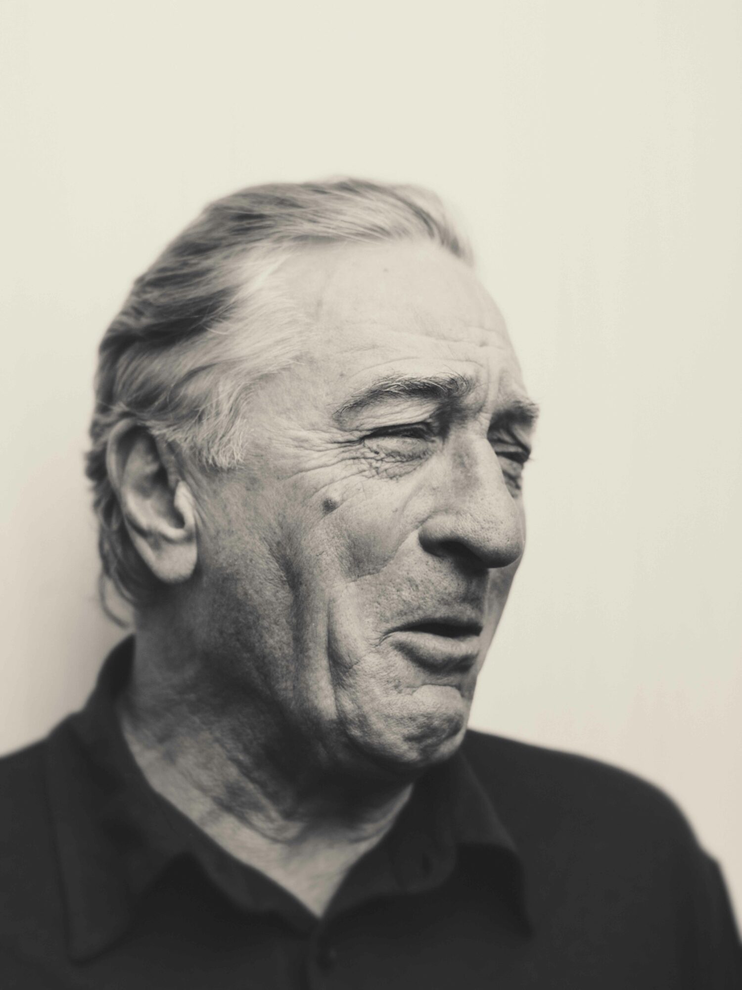 Black and white portrait of an elderly man with closed eyes and a serious expression, wearing a dark shirt.
