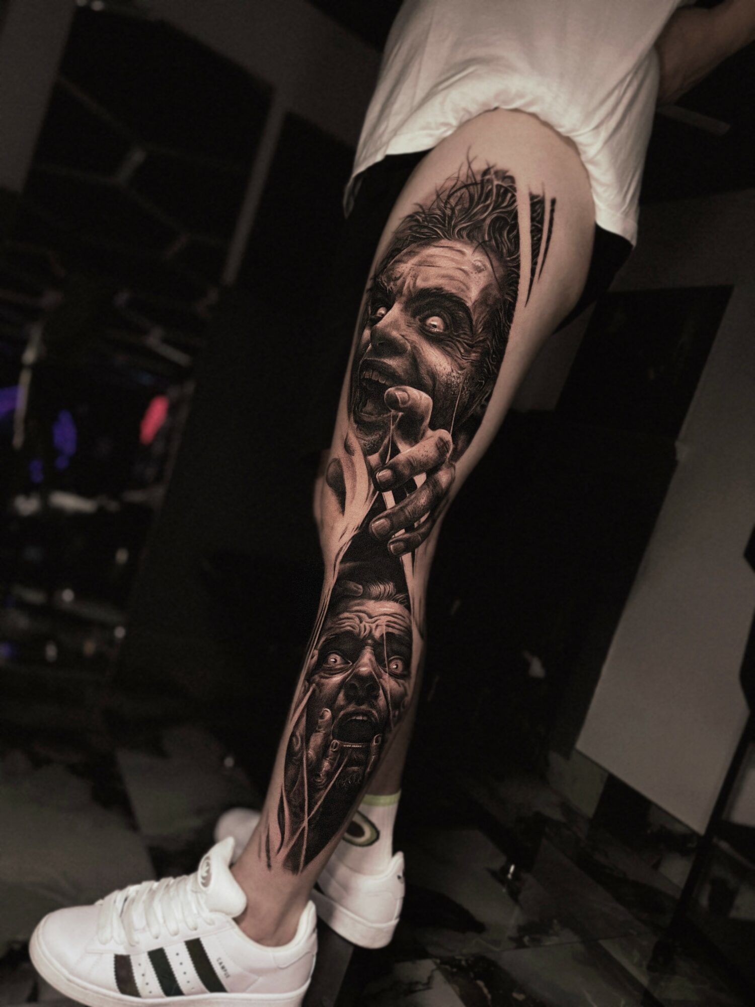 Tattoo of two faces with intense expressions on a person's thigh, with detailed shading and realistic features.