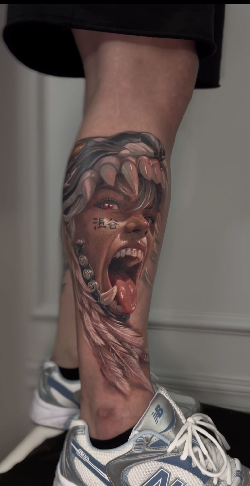 Tattoo of a fierce, open-mouthed creature with sharp teeth on a person's lower leg.