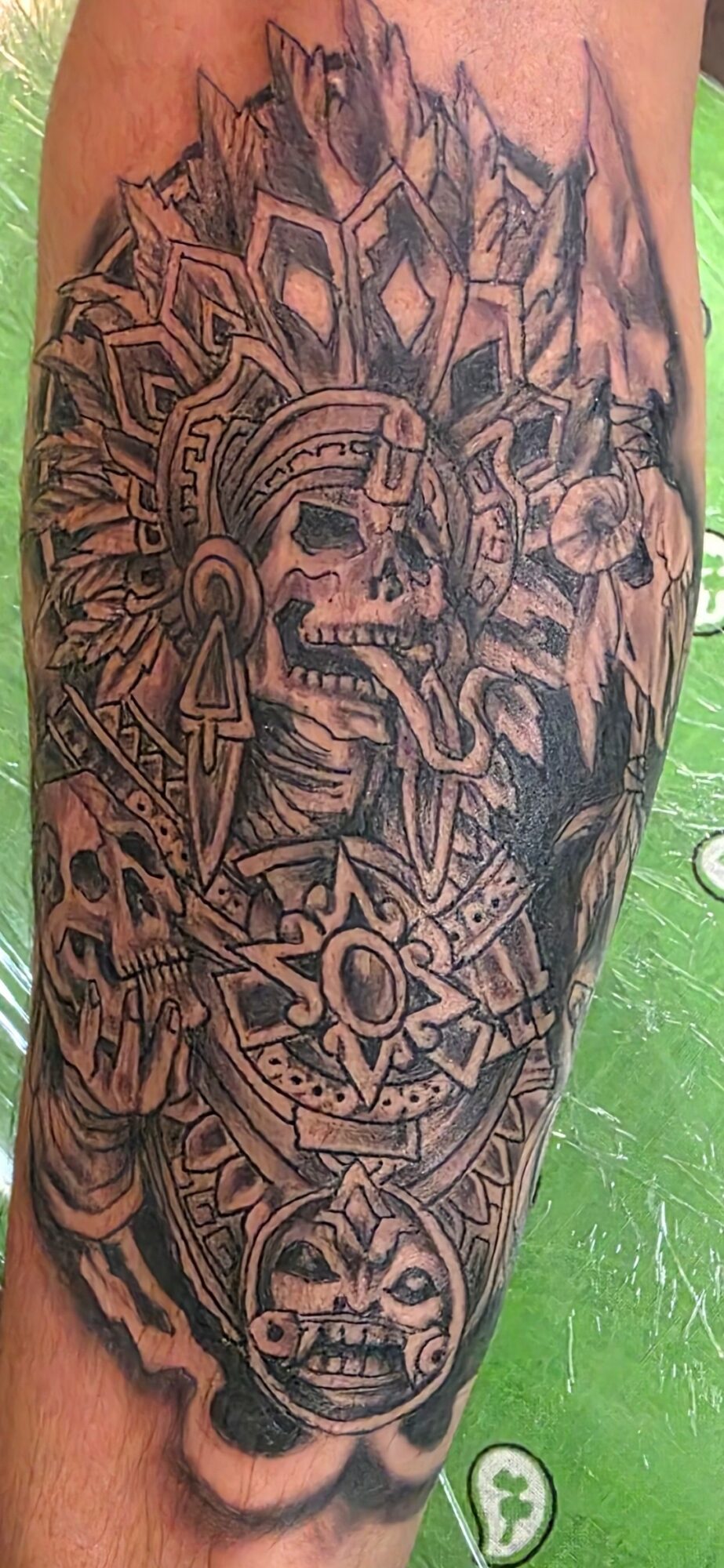 Tattoo of a skull with geometric patterns, a face, and intricate designs on skin, black ink, detailed shading.