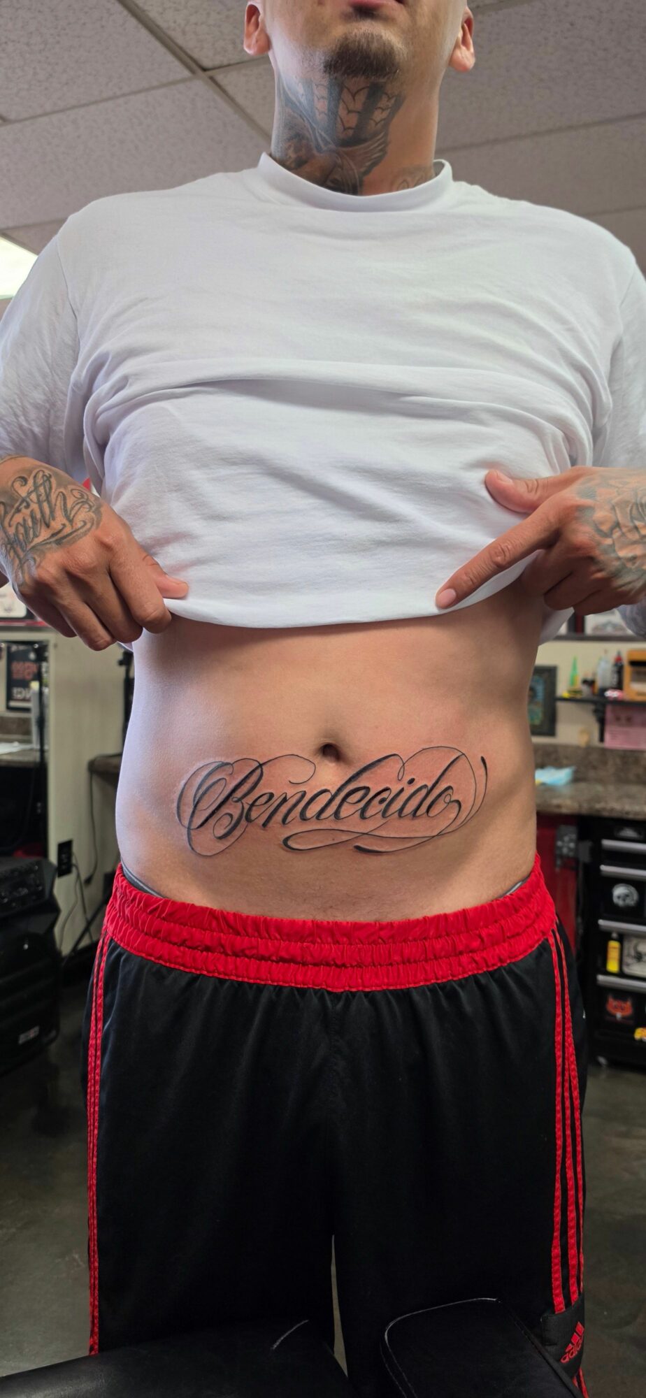 Person lifting shirt to reveal tattoo on abdomen, with a dog partially visible in the background.