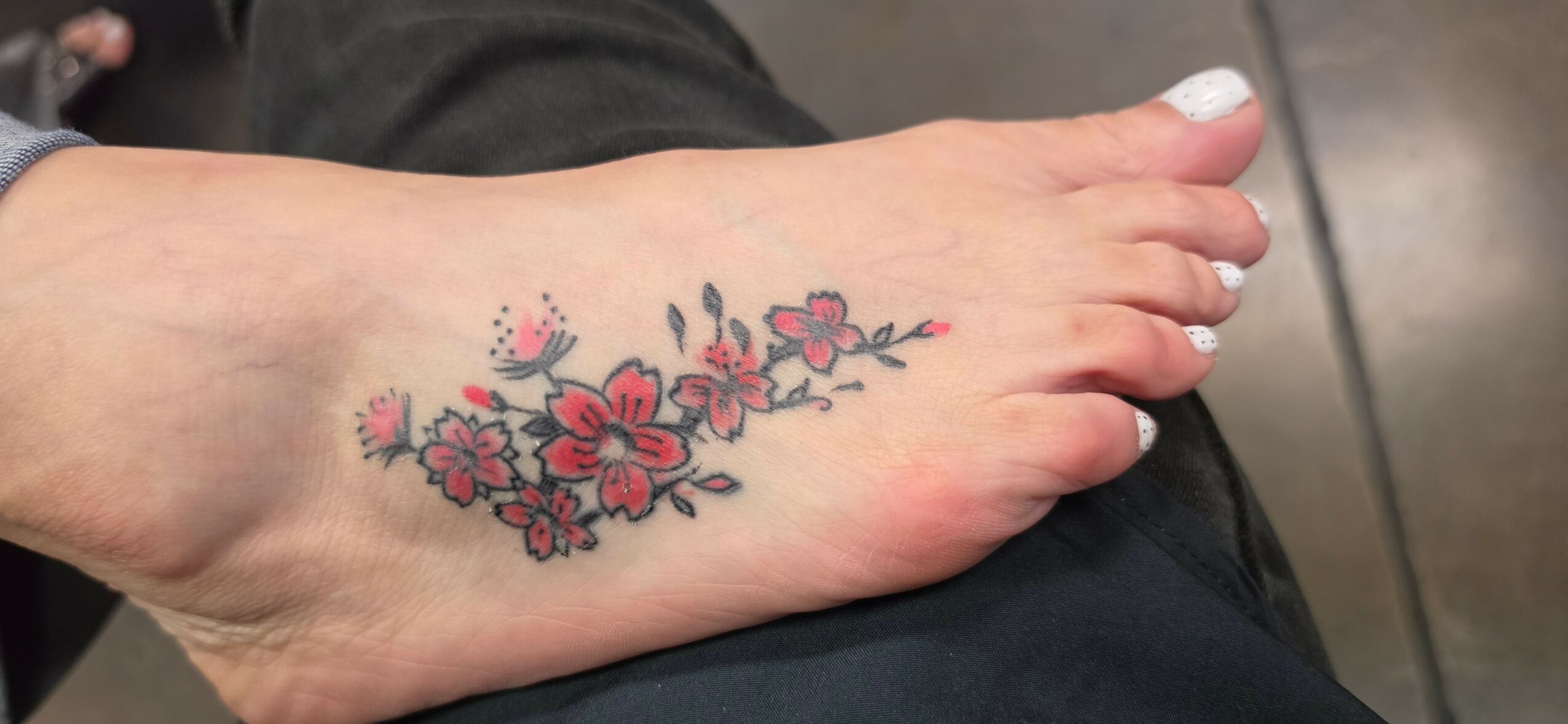 Foot with a colorful floral tattoo on the top, featuring pink and red flowers with green leaves.