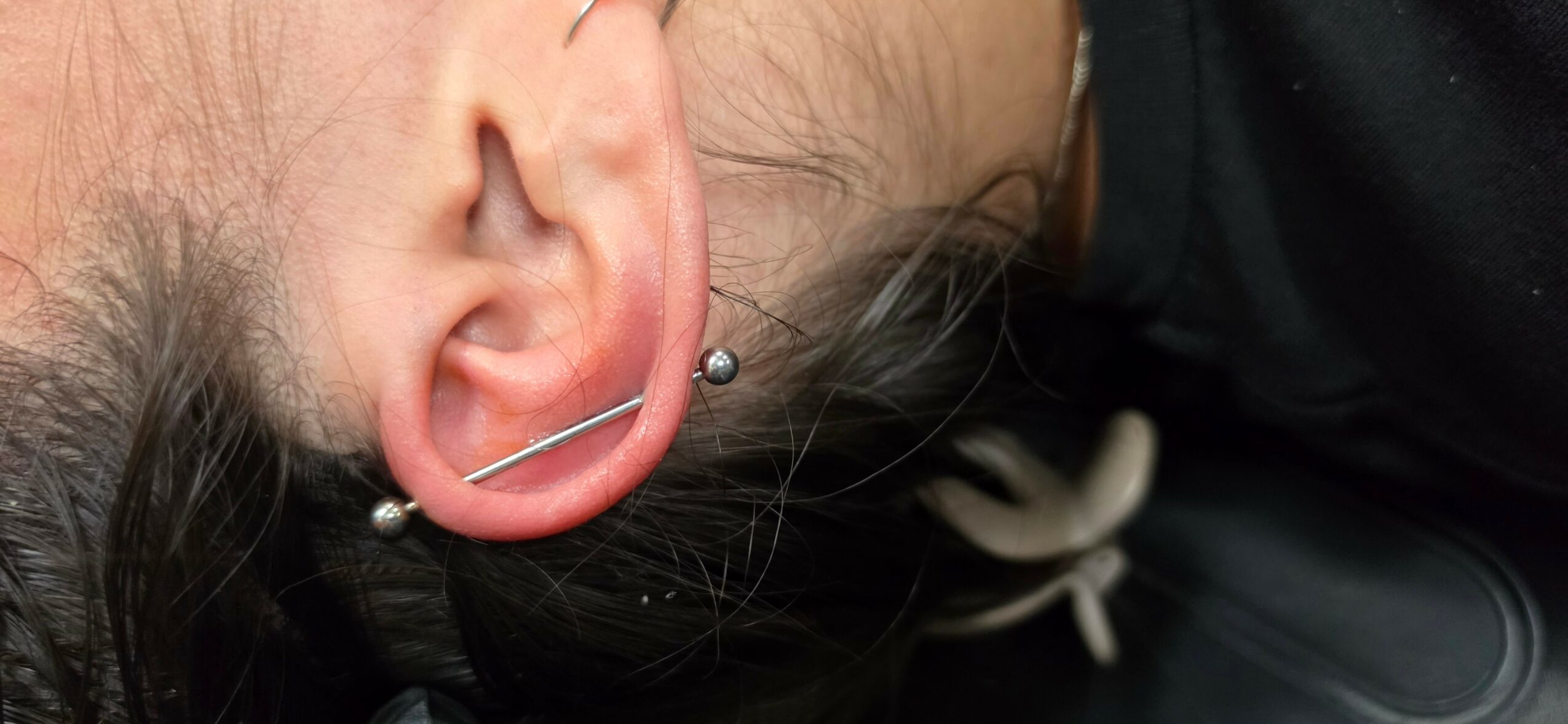 Close-up of a person's ear with multiple piercings, including a hoop and a stud, and dark hair partially visible.
