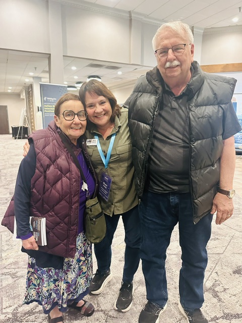 Three people standing together indoors, smiling, with a background of a modern building interior.