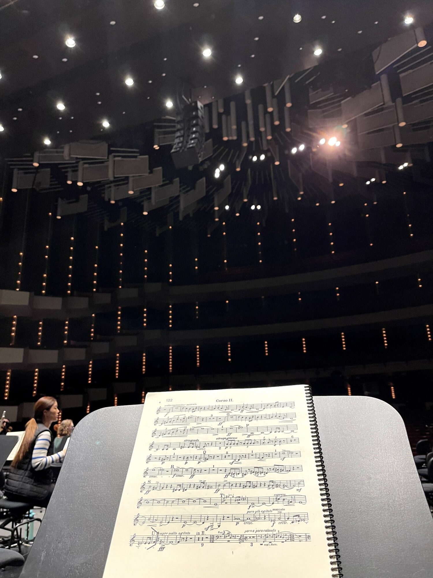 Music sheet on a stand in a concert hall with a ceiling decorated with hanging geometric shapes and small lights.