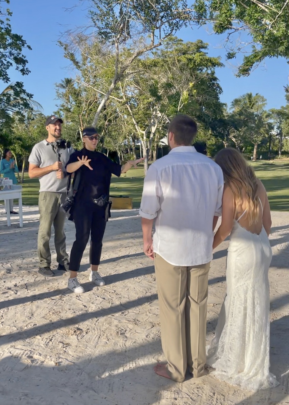 Group of four people outdoors, two facing each other and two with backs to the camera, in a park with trees and blue sky