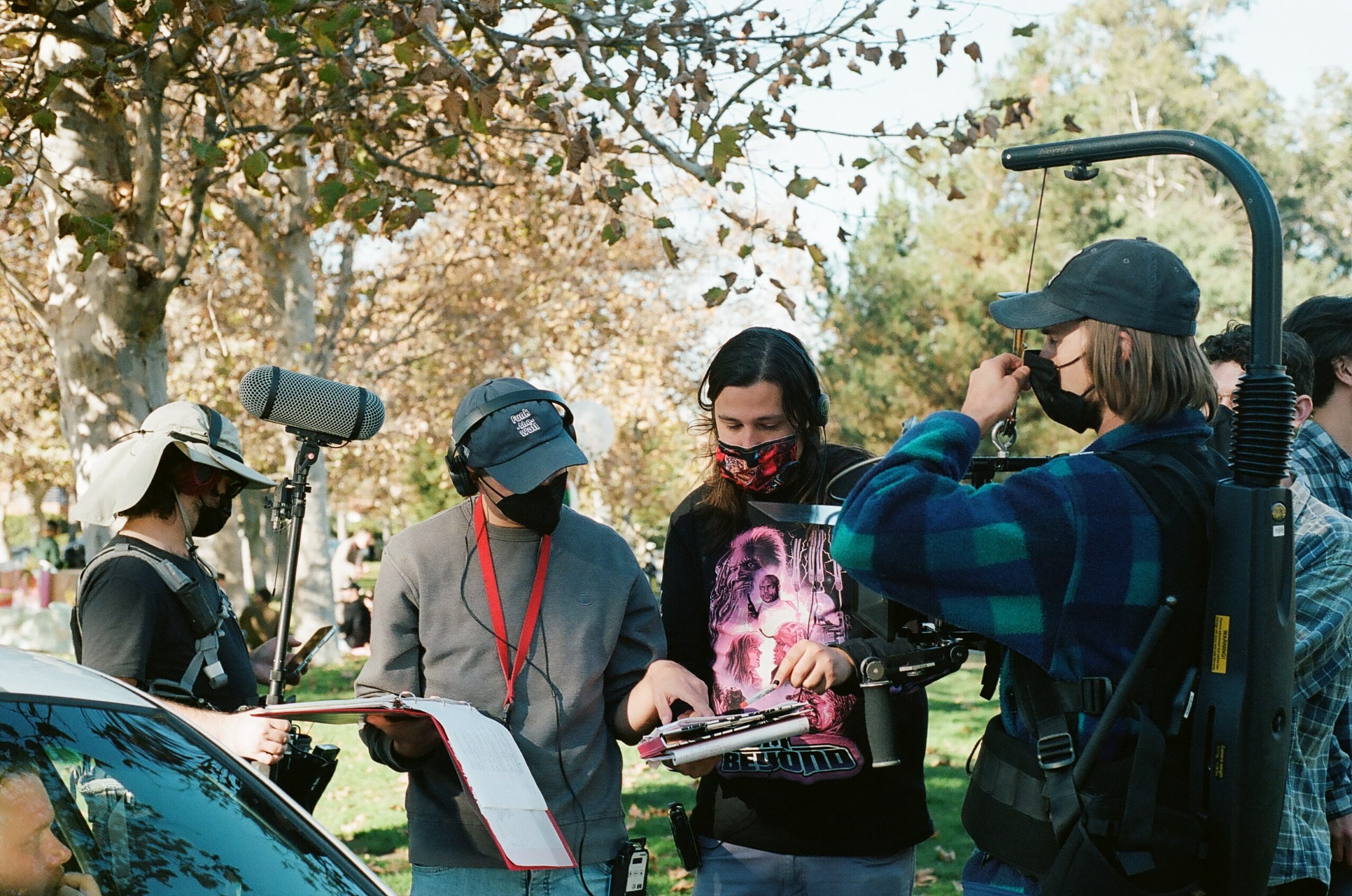 Group of people outdoors, some with cameras and equipment, trees in background, daytime.