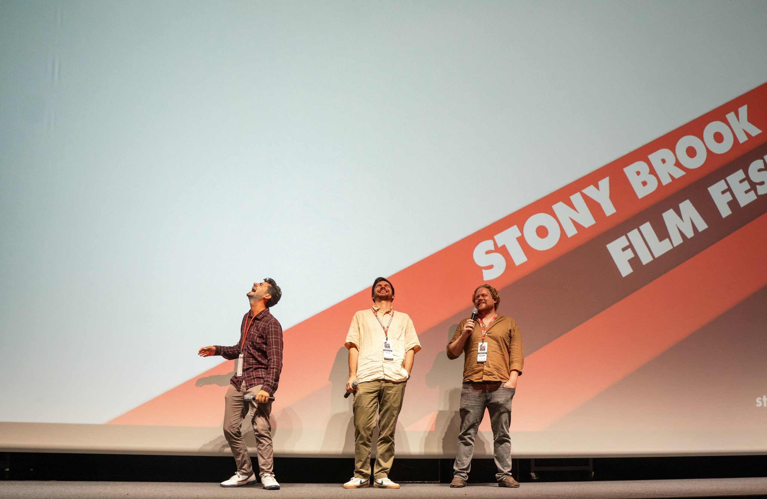 Three people standing on stage in front of a large screen with text reading 'Stony Brook Film Fest'.