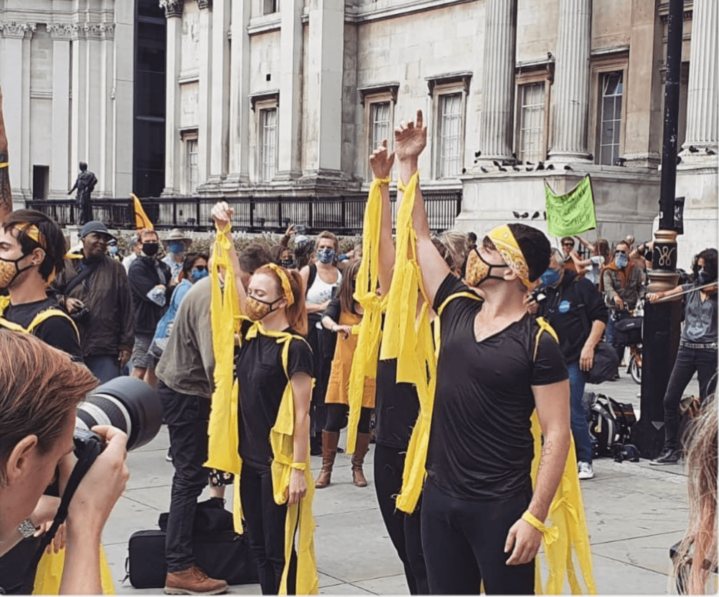 Group of people wearing yellow and black clothing and masks, participating in a protest or demonstration outdoors.