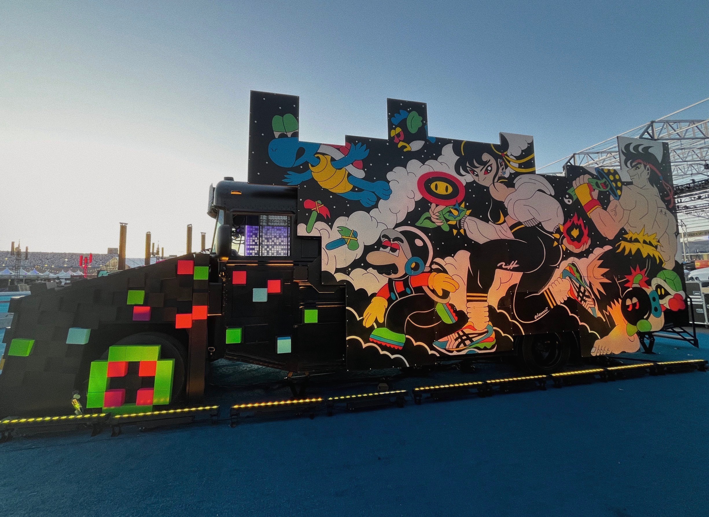 Colorful pixel art and mural on a large structure outdoors, with a clear sky and distant cityscape in background.