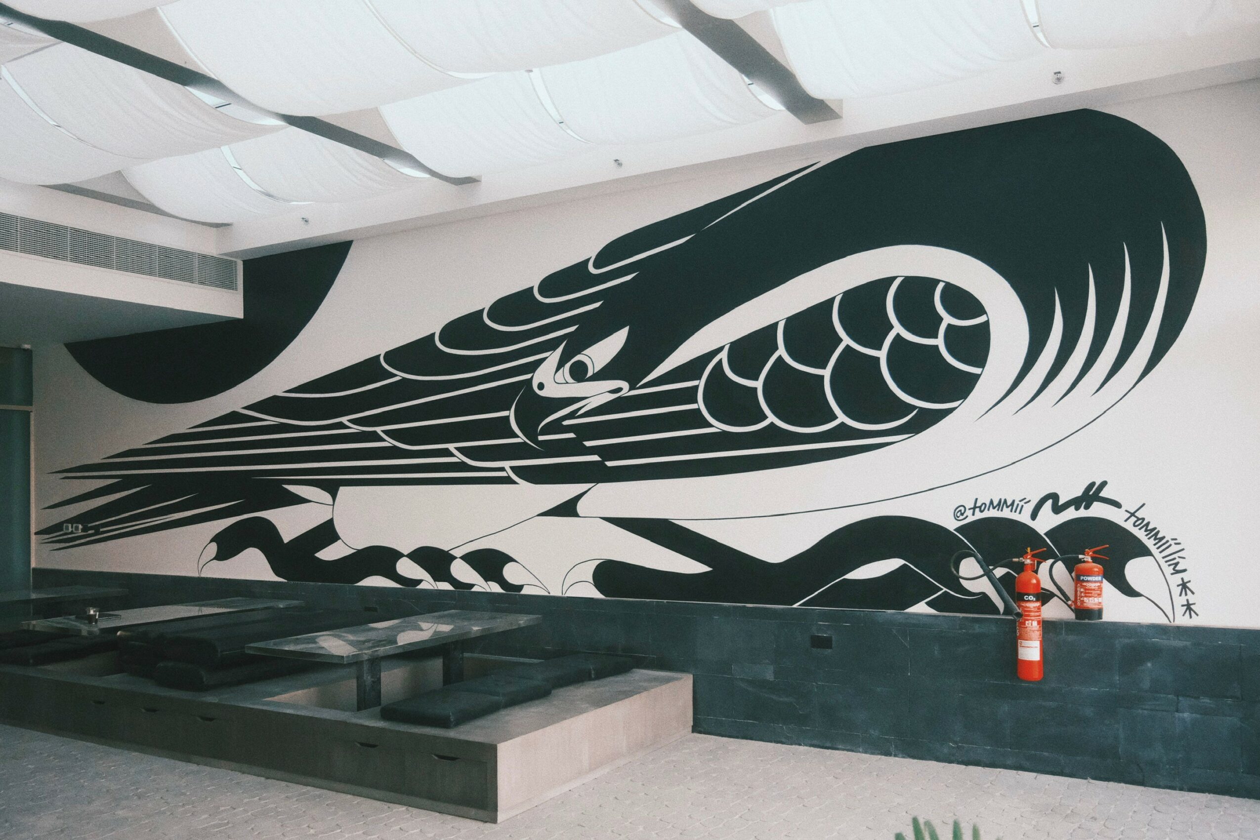 Large black and white mural of a stylized snake with intricate patterns on a wall, with fire extinguishers nearby.